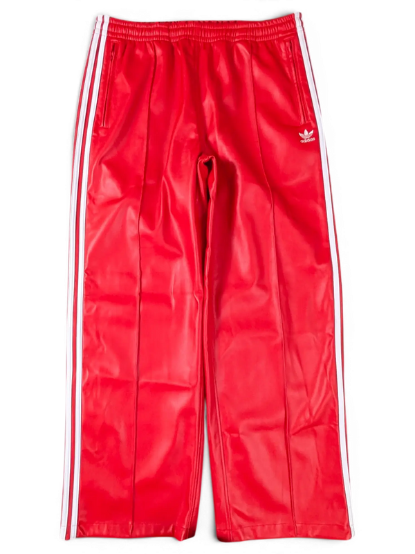 JAKE & IPI red Adidas track pants with white side stripes and embroidered logo on a green background