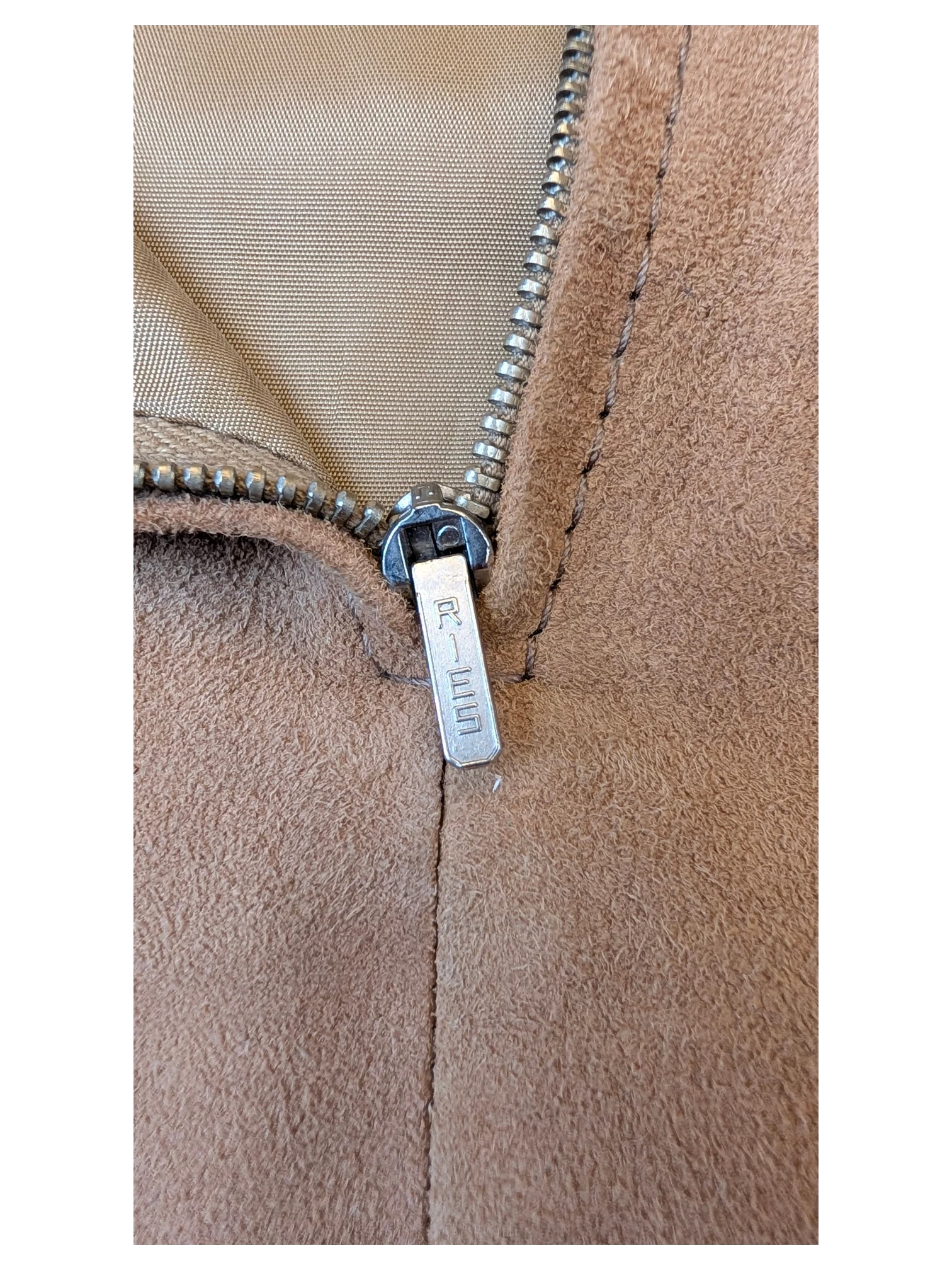 Close-up of a JAKE & IPI beige suede leather skirt featuring a silver metal zipper with RIES branding.
