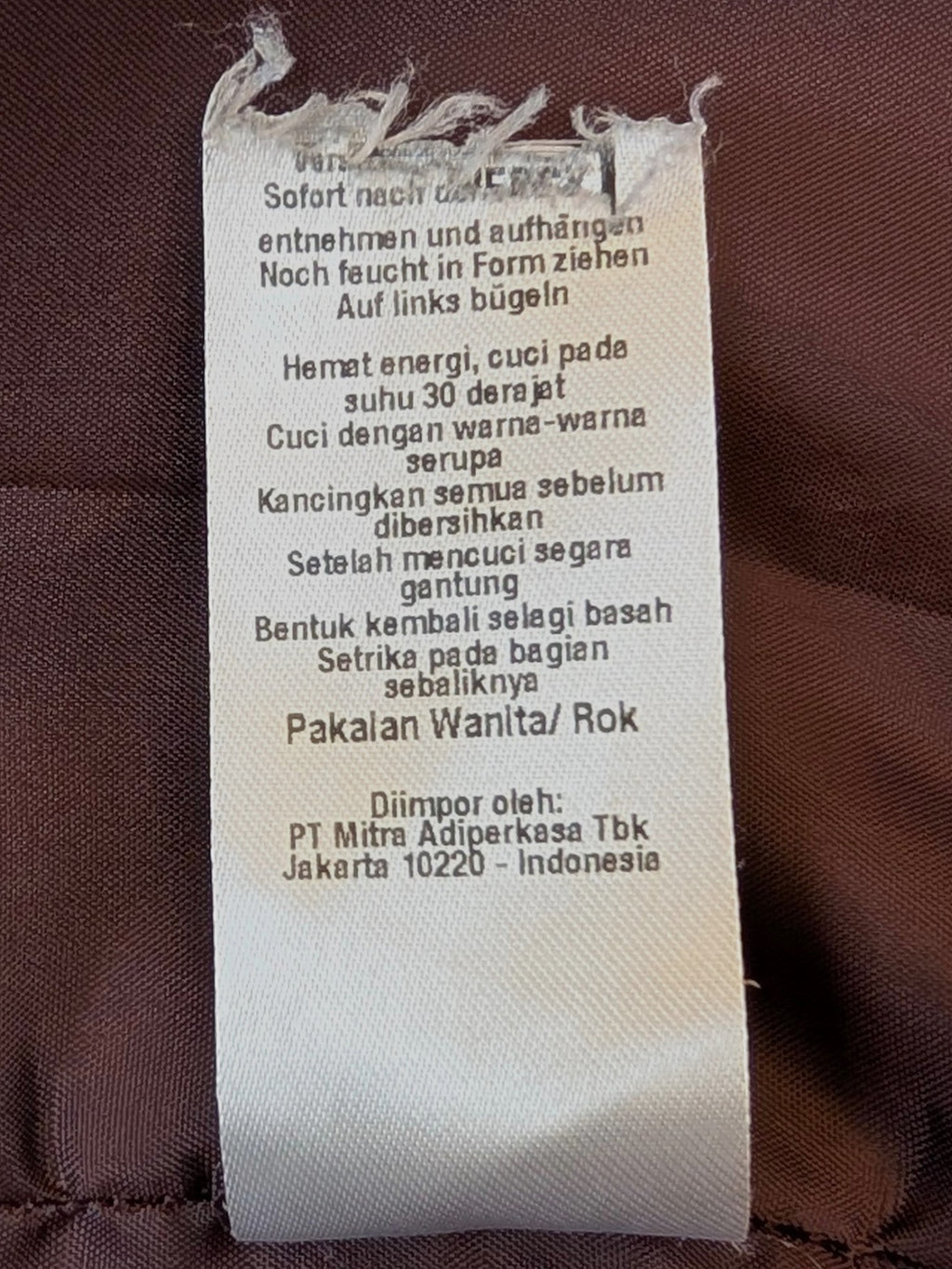 JAKE & IPI embroidered faux leather mini skirt care label with washing instructions on brown fabric background.