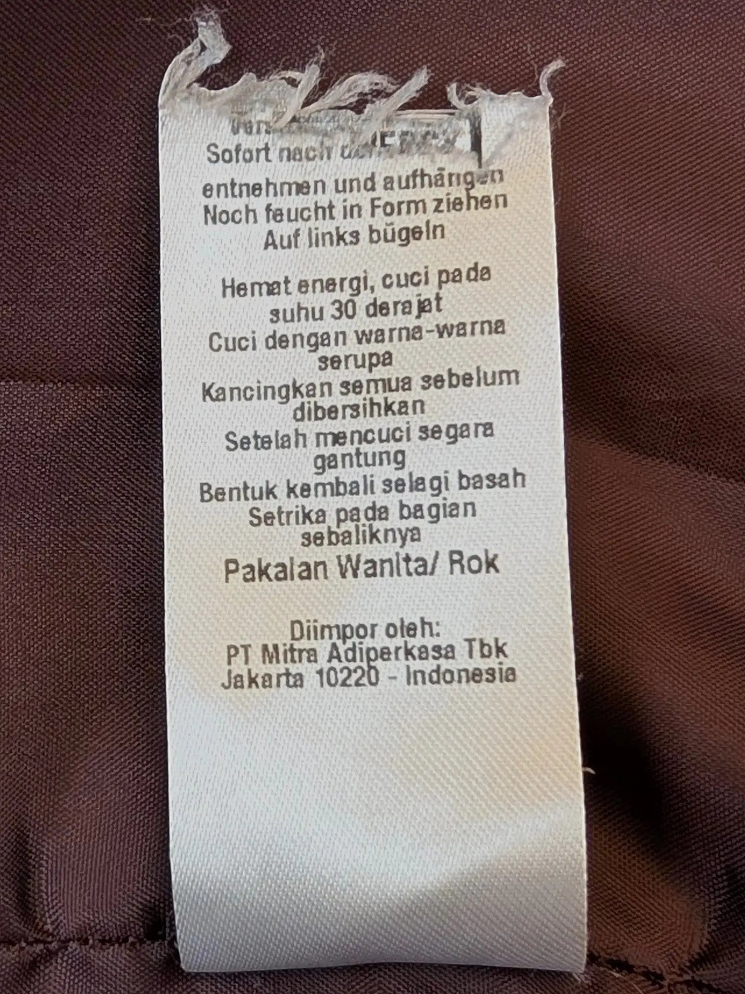 JAKE & IPI embroidered faux leather mini skirt care label with washing instructions on brown fabric background.