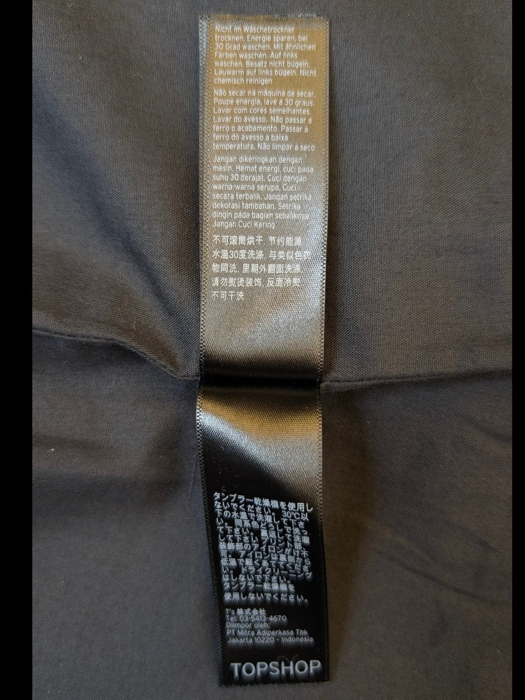 Care label for JAKE & IPI TOPSHOP buckled faux leather mini skirt with multi-language washing instructions.