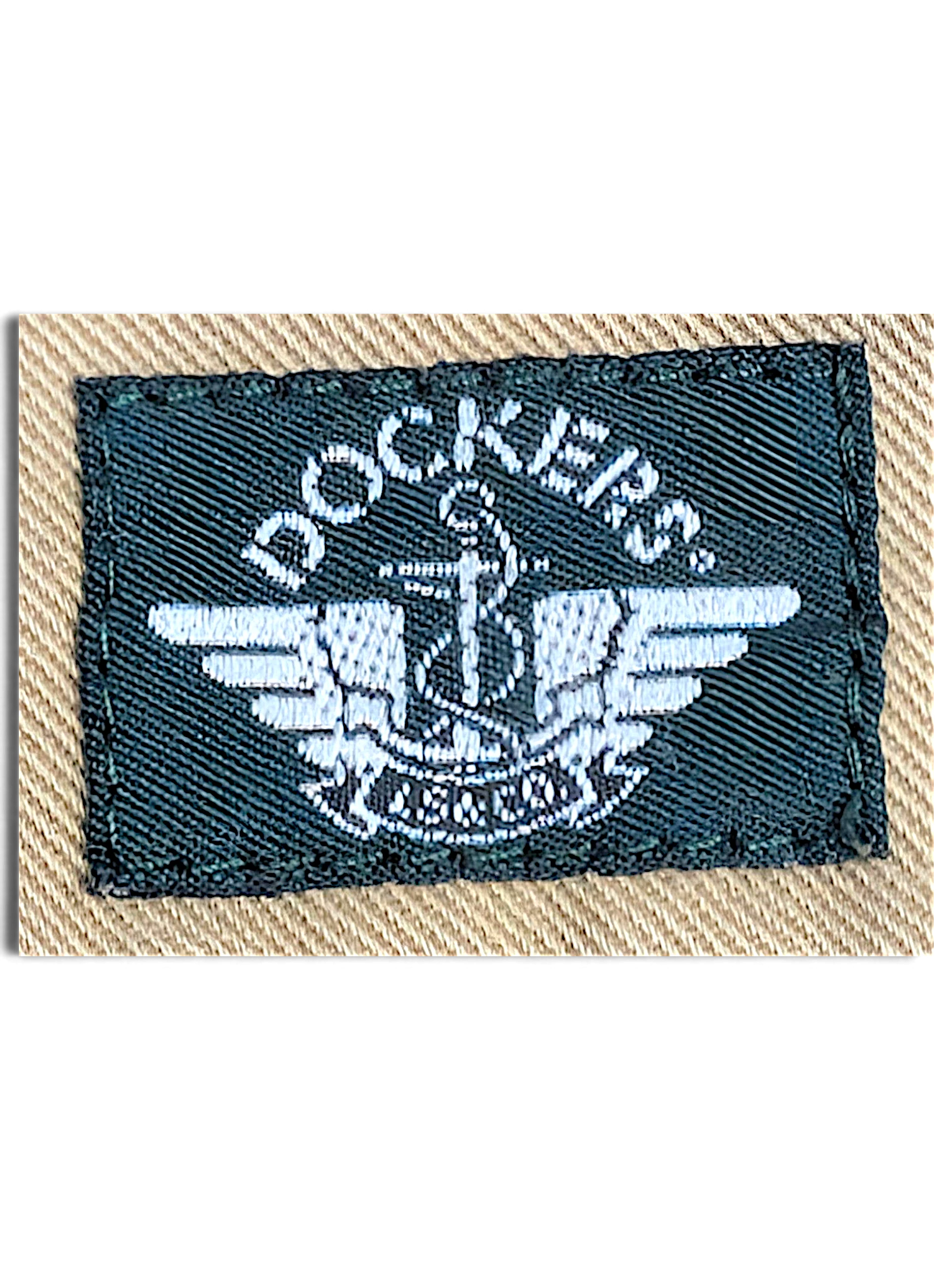 JAKE & IPI Dockers brand logo label embroidered in white on a dark green patch against beige cotton fabric