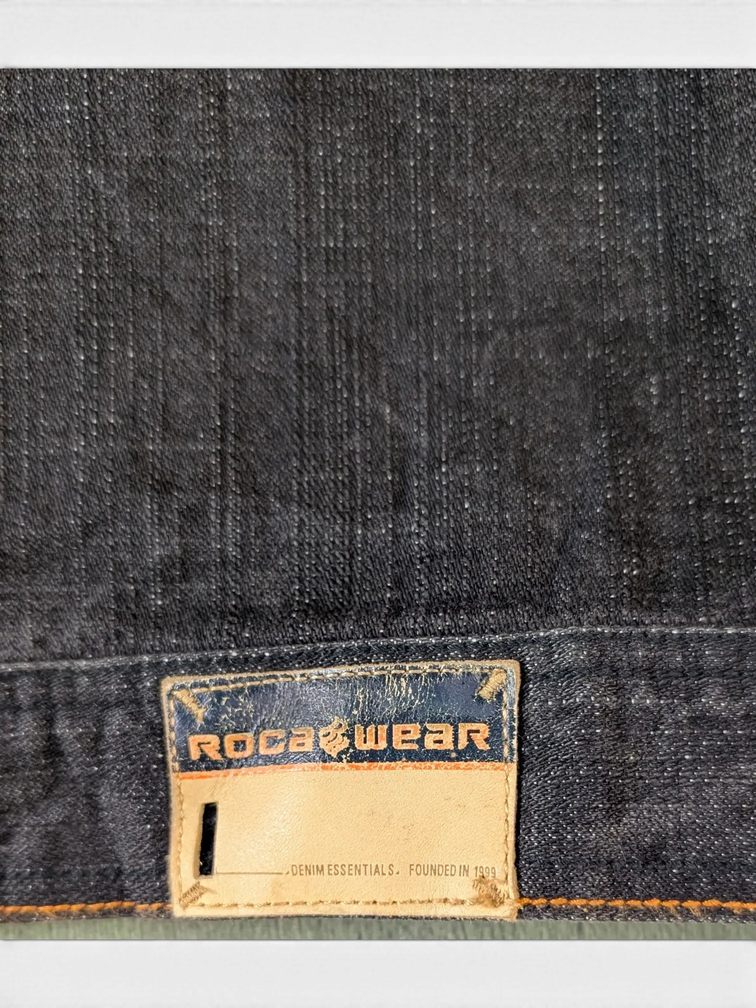 JAKE & IPI Rocawear dark wash denim jacket with leather logo patch and "DENIM ESSENTIALS. FOUNDED IN 1999" text.