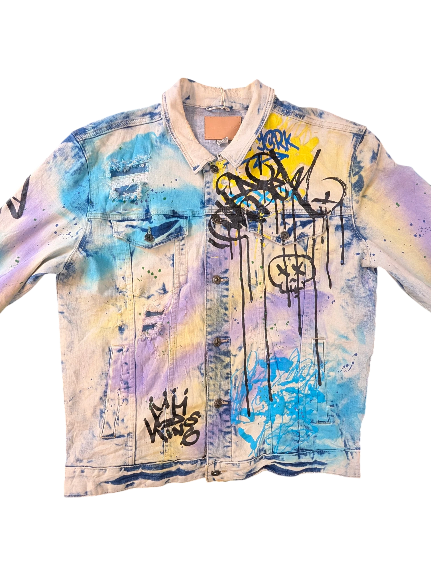 JAKE & IPI Smoke Rise denim jacket with graffiti print, distressed details, and tie-dye effect in blue, yellow, and purple.