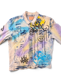 JAKE & IPI Smoke Rise denim jacket with graffiti print, distressed details, and tie-dye effect in blue, yellow, and purple.