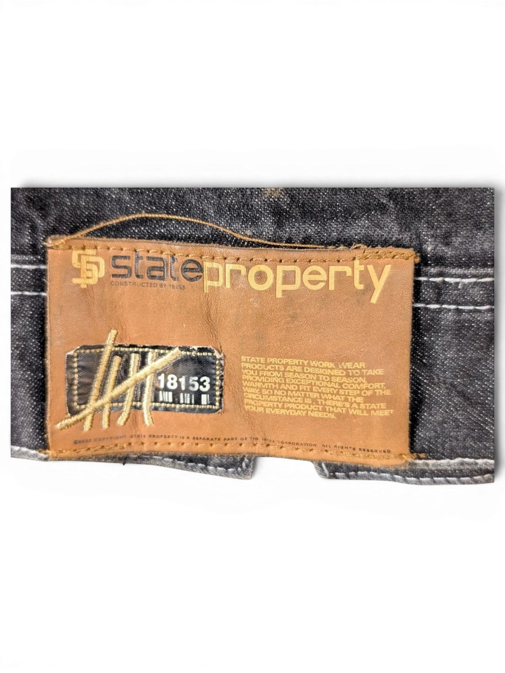 JAKE & IPI State Property dark wash denim jacket with brown leather logo patch and white stitching.