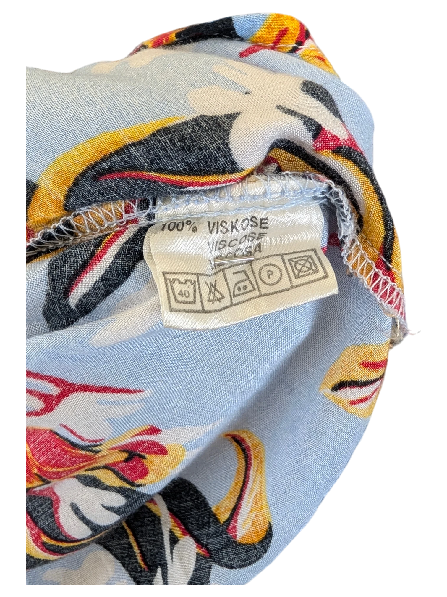 JAKE & IPI vintage Hawaiian shirt label showing 100% viscose material and care instructions on light blue floral fabric