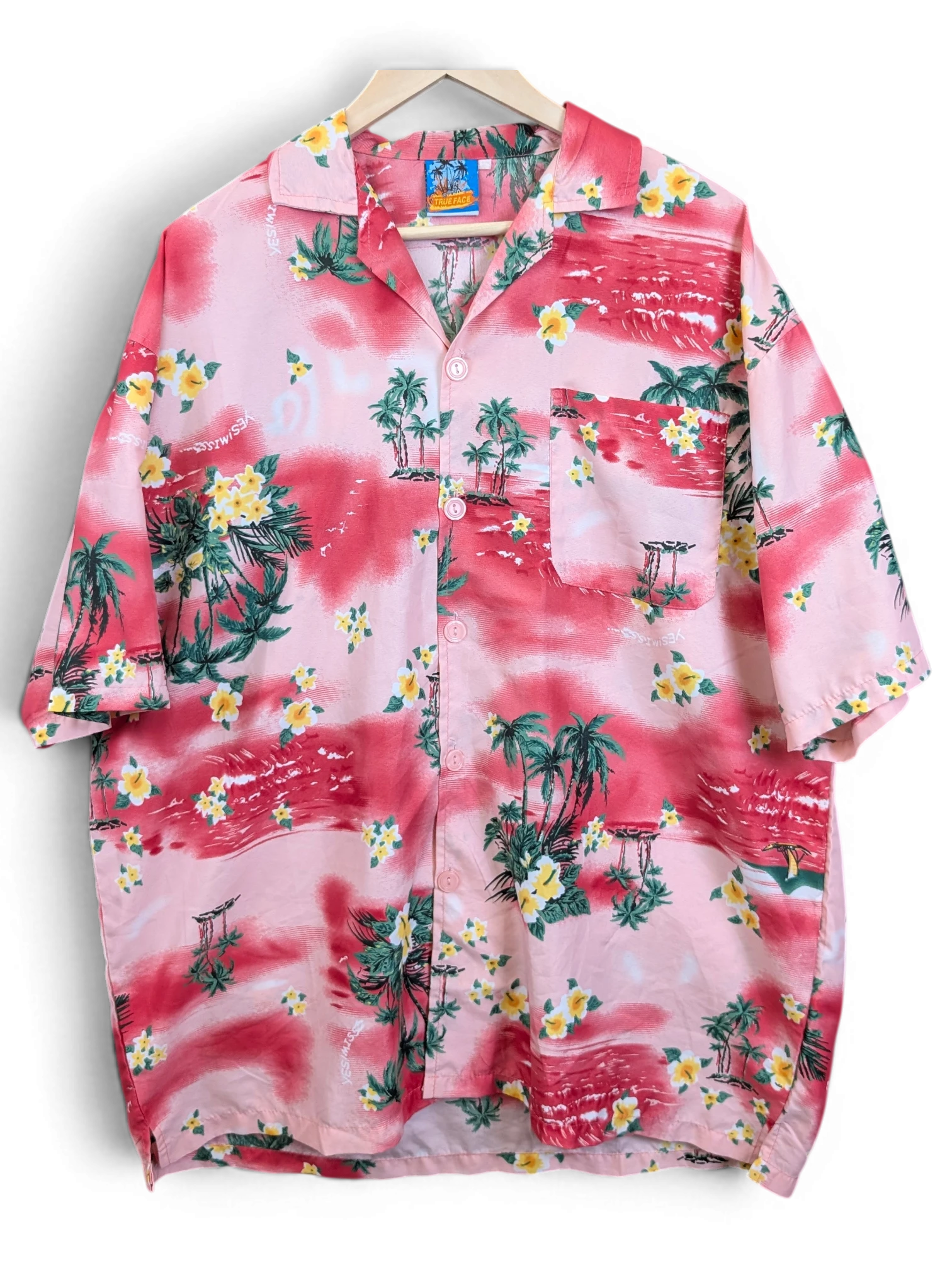 JAKE & IPI True Face Hawaiian shirt in pink with yellow floral and tropical palm tree print on a wooden hanger