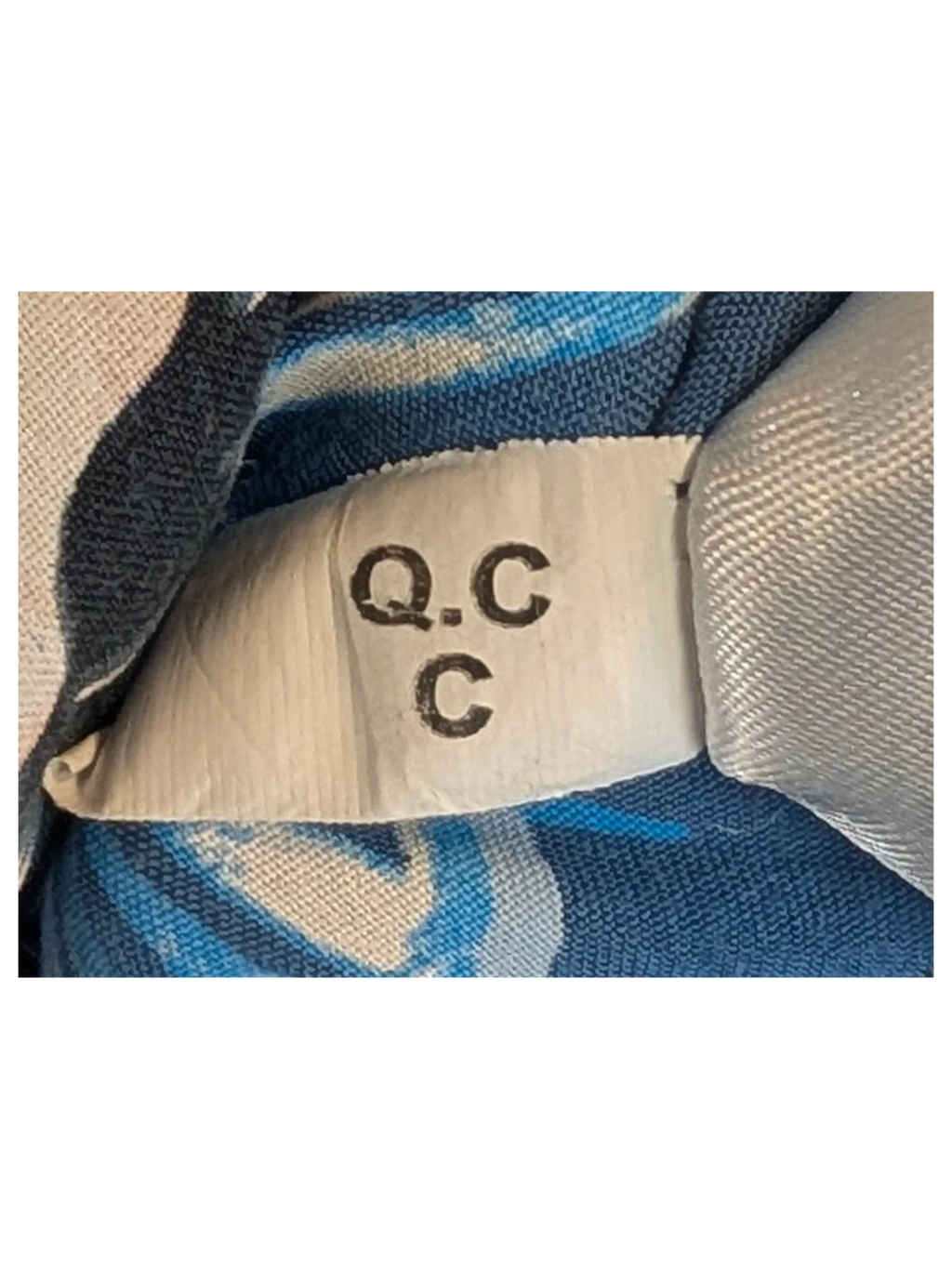 JAKE & IPI Angelo Litrico Hawaiian shirt fabric detail showing a Q.C.C quality control tag on blue patterned fabric