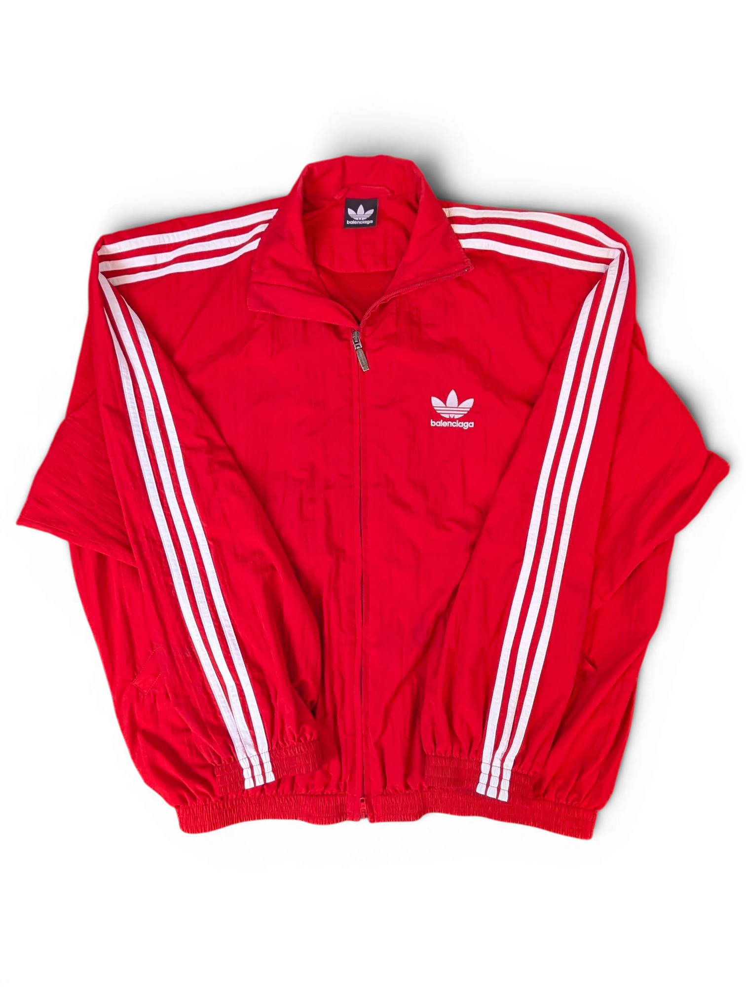JAKE & IPI Balenciaga x Adidas red zip-up track jacket with white three-stripe detailing and dual branding.