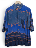 JAKE & IPI Bali Eva Hawaiian shirt in blue with orange wave patterns and a chest pocket hanging on a hanger