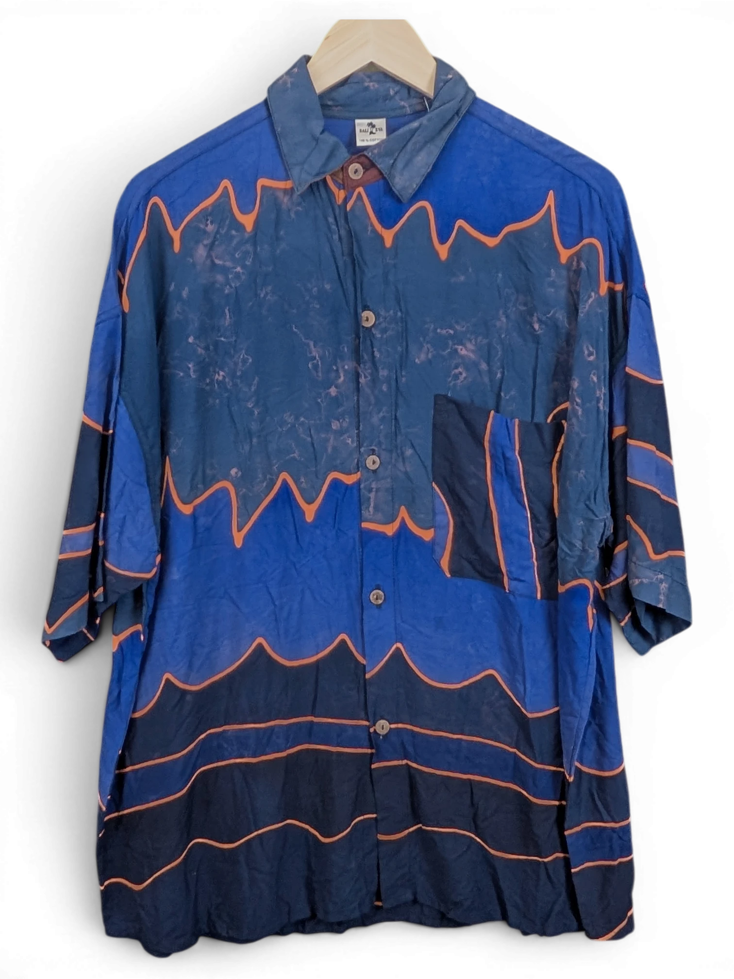 JAKE & IPI Bali Eva Hawaiian shirt in blue with orange wave patterns and a chest pocket hanging on a hanger