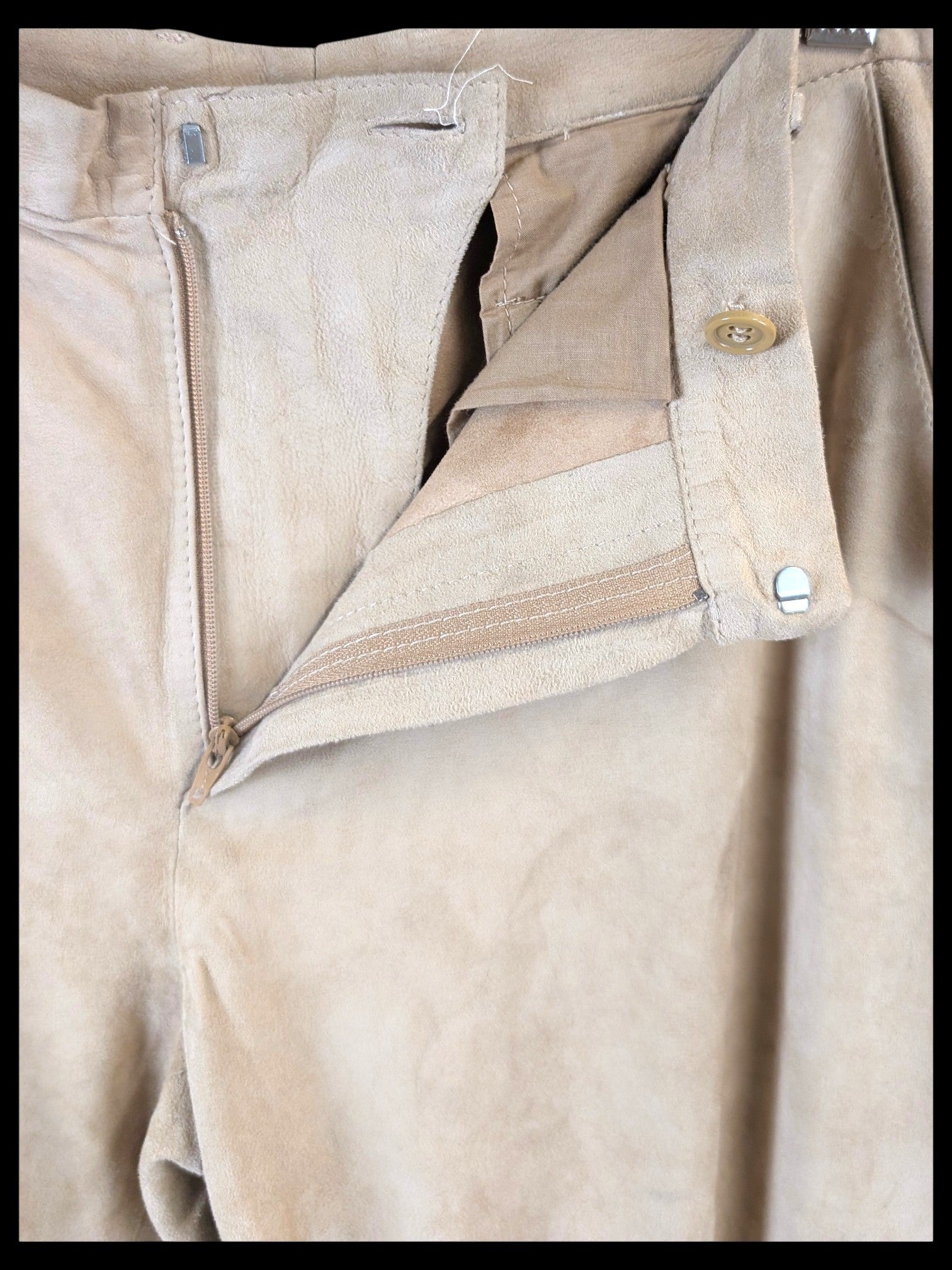 JAKE & IPI beige suede leather pants featuring a button and zipper fly closure, hanging on a wooden hanger.