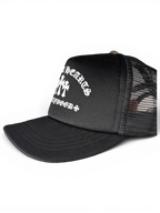 JAKE & IPI black Chrome Hearts trucker hat with white gothic lettering and cross embroidery on the front panel