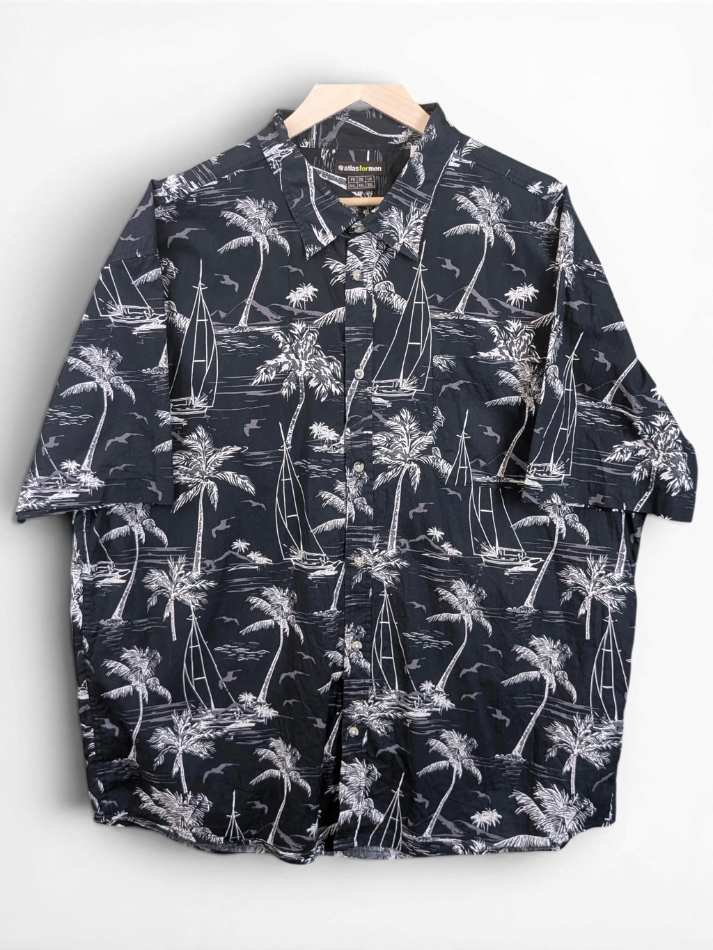JAKE & IPI Atlas For Men black and white Hawaiian shirt with palm tree and sailboat print on a wooden hanger