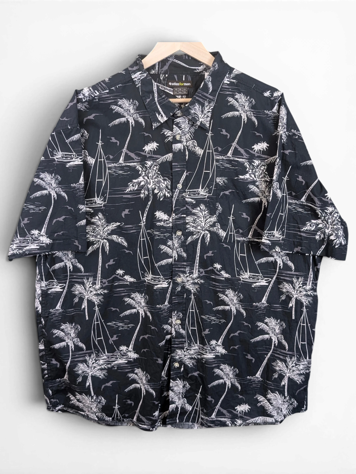 JAKE & IPI Atlas For Men black and white Hawaiian shirt with palm tree and sailboat print on a wooden hanger