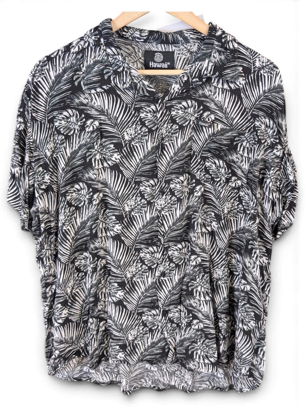JAKE & IPI black and white Hawaiian shirt with a tropical palm leaf print and short sleeves on a wooden hanger.