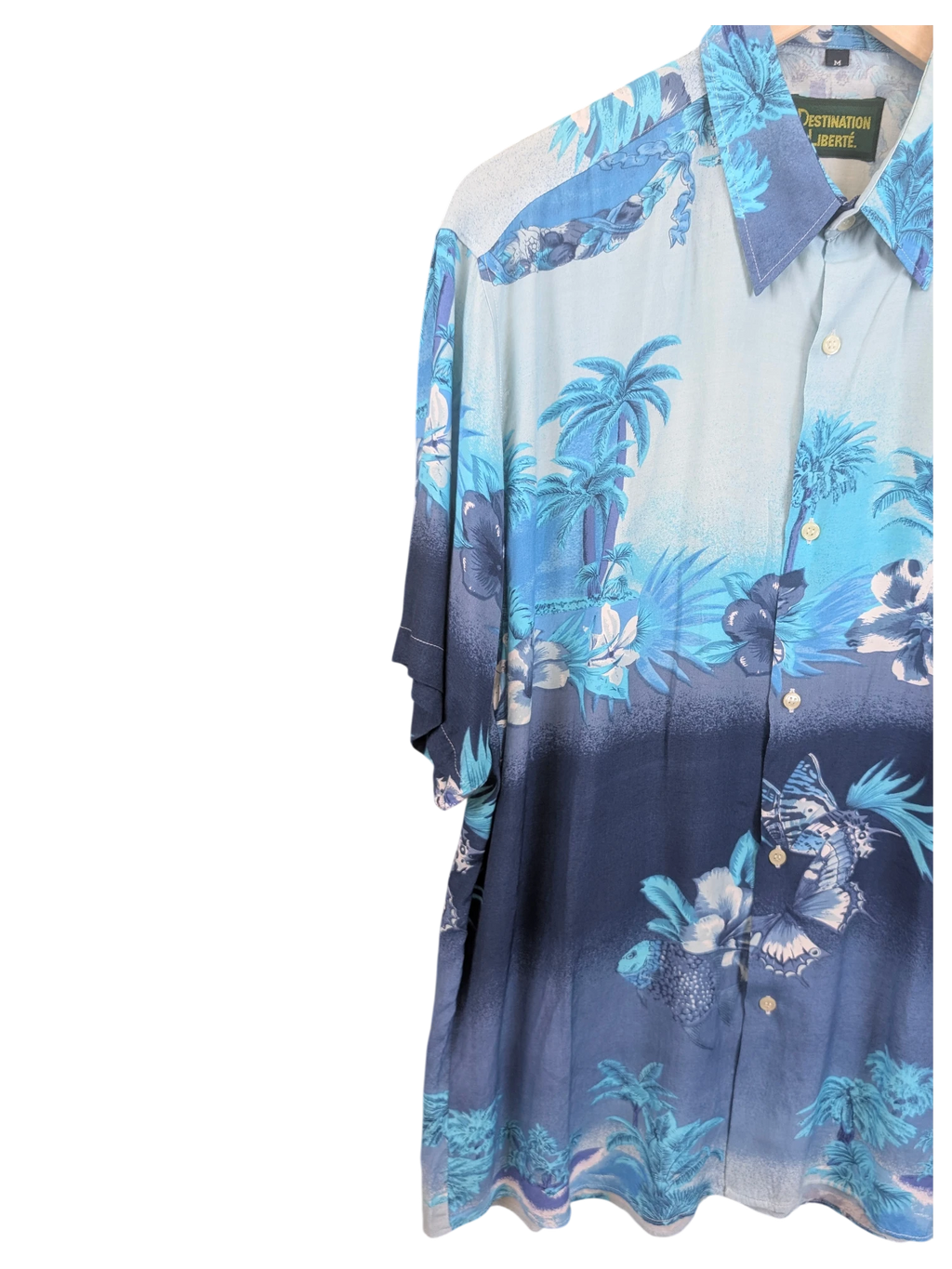 JAKE & IPI Destination Liberté Hawaiian shirt in blue with tropical palm tree and butterfly print on a hanger
