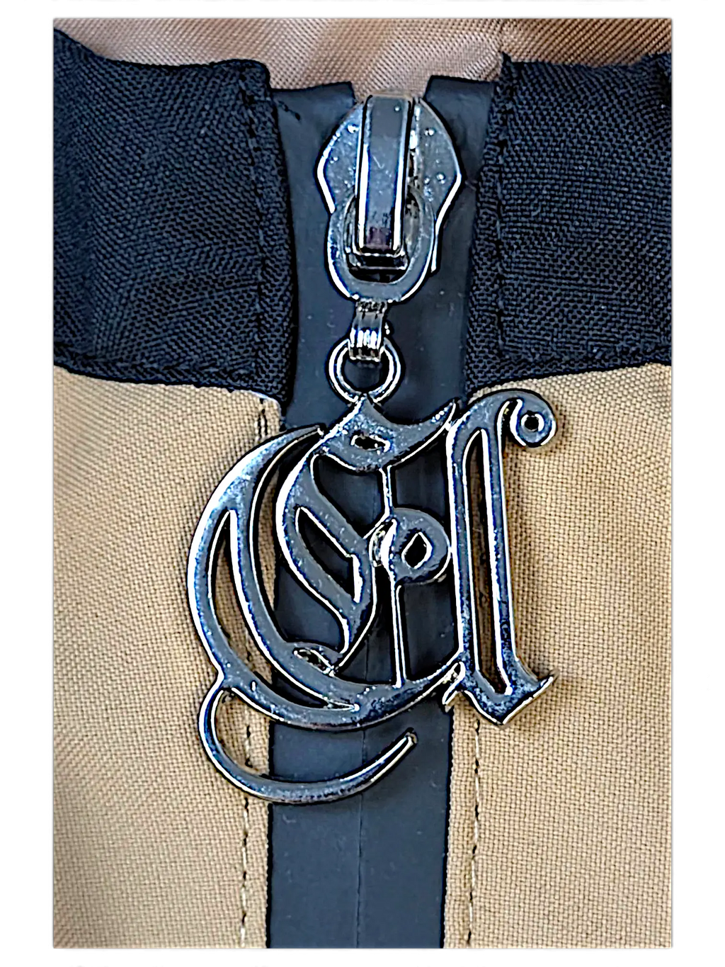 Close-up of a JAKE & IPI brown jacket featuring a silver metallic logo zipper pull with intricate script detailing.
