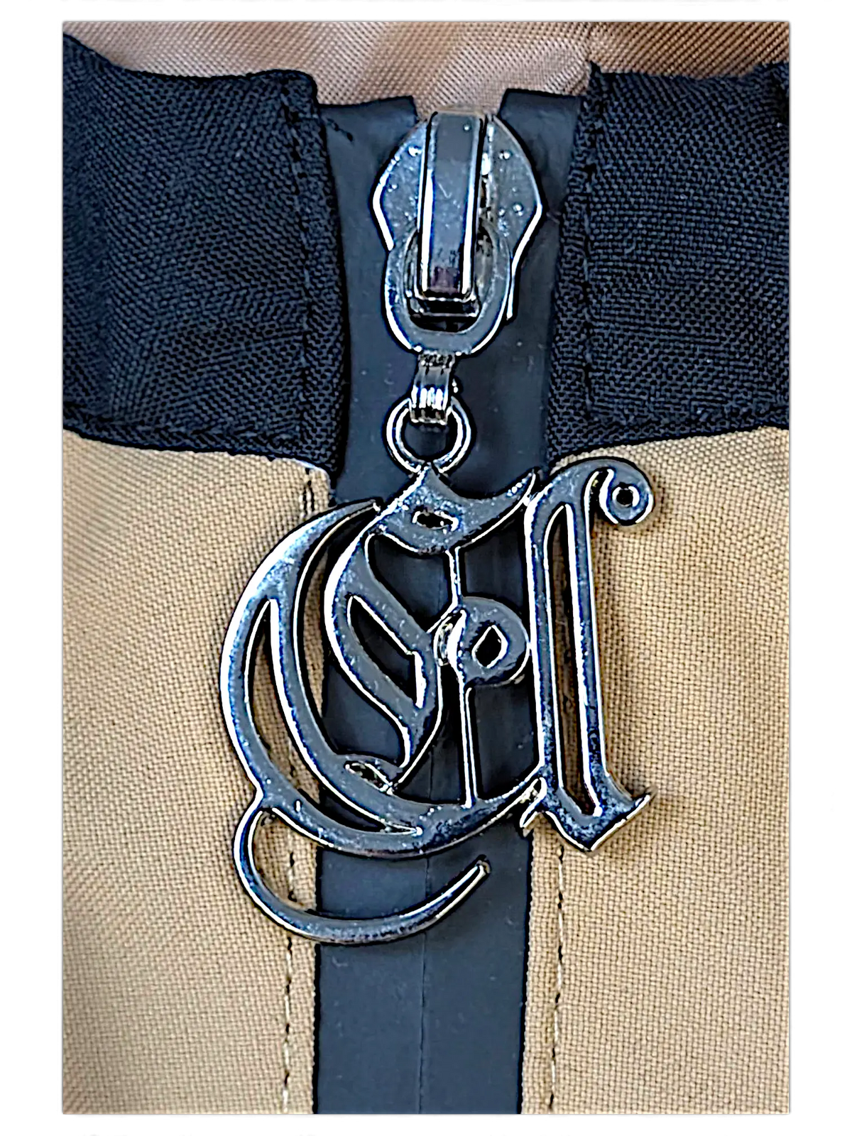Close-up of a JAKE & IPI brown jacket featuring a silver metallic logo zipper pull with intricate script detailing.
