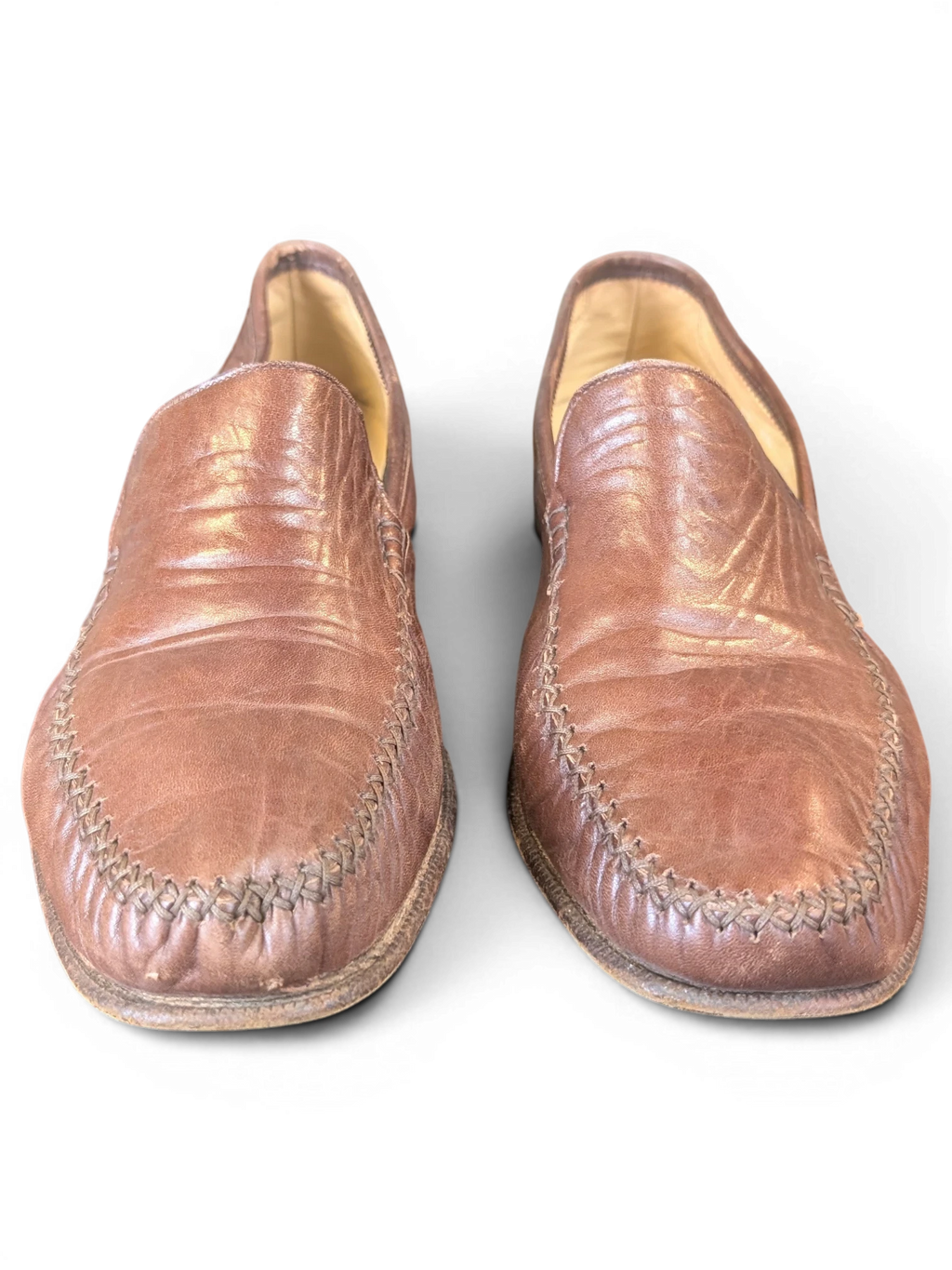 JAKE & IPI brown leather loafers with decorative whipstitch detailing on the toe, displayed on a wooden surface.