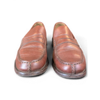 JAKE & IPI brown leather penny loafers with classic moccasin stitching on a wooden surface
