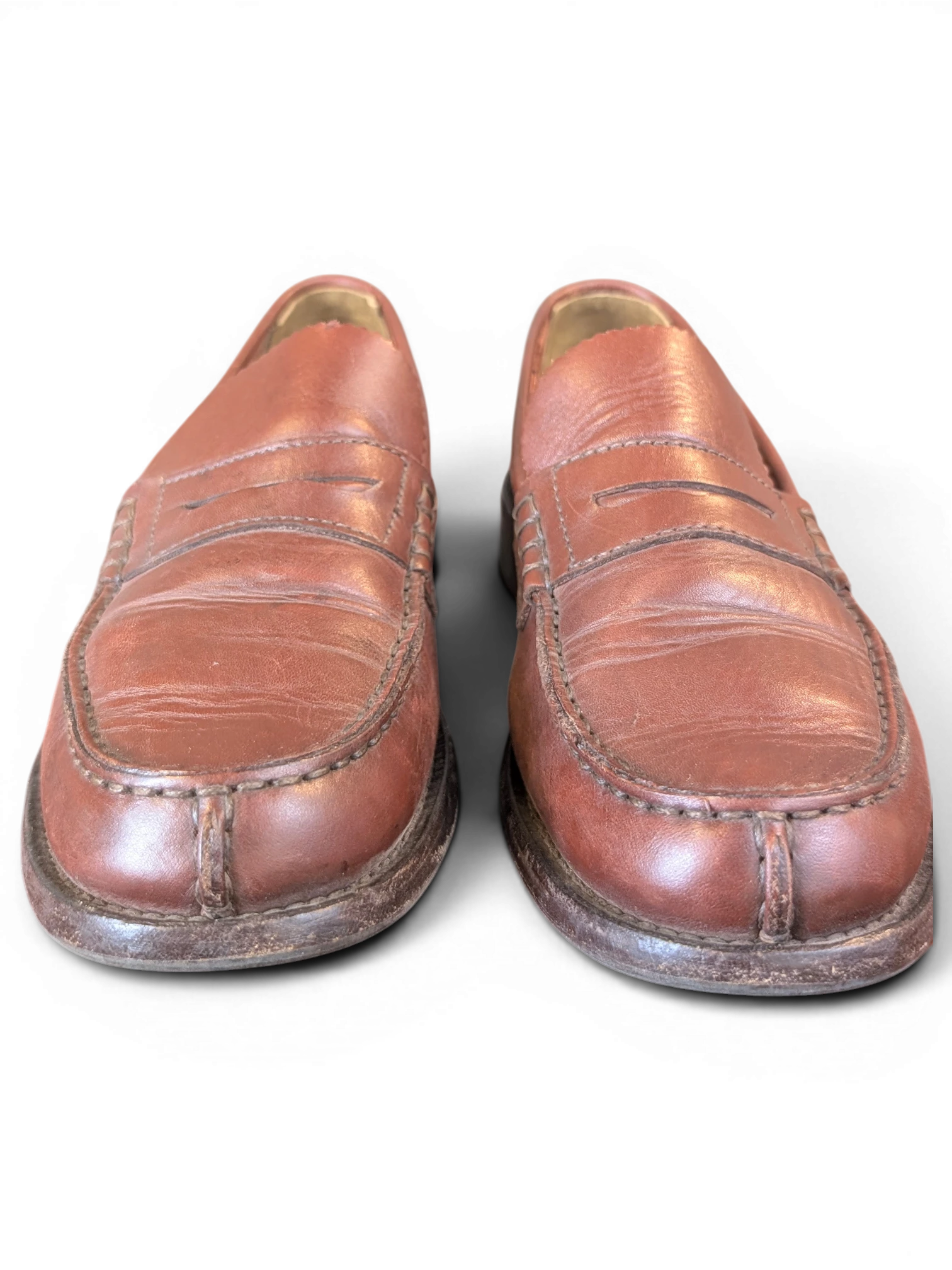 JAKE & IPI brown leather penny loafers with classic moccasin stitching on a wooden surface
