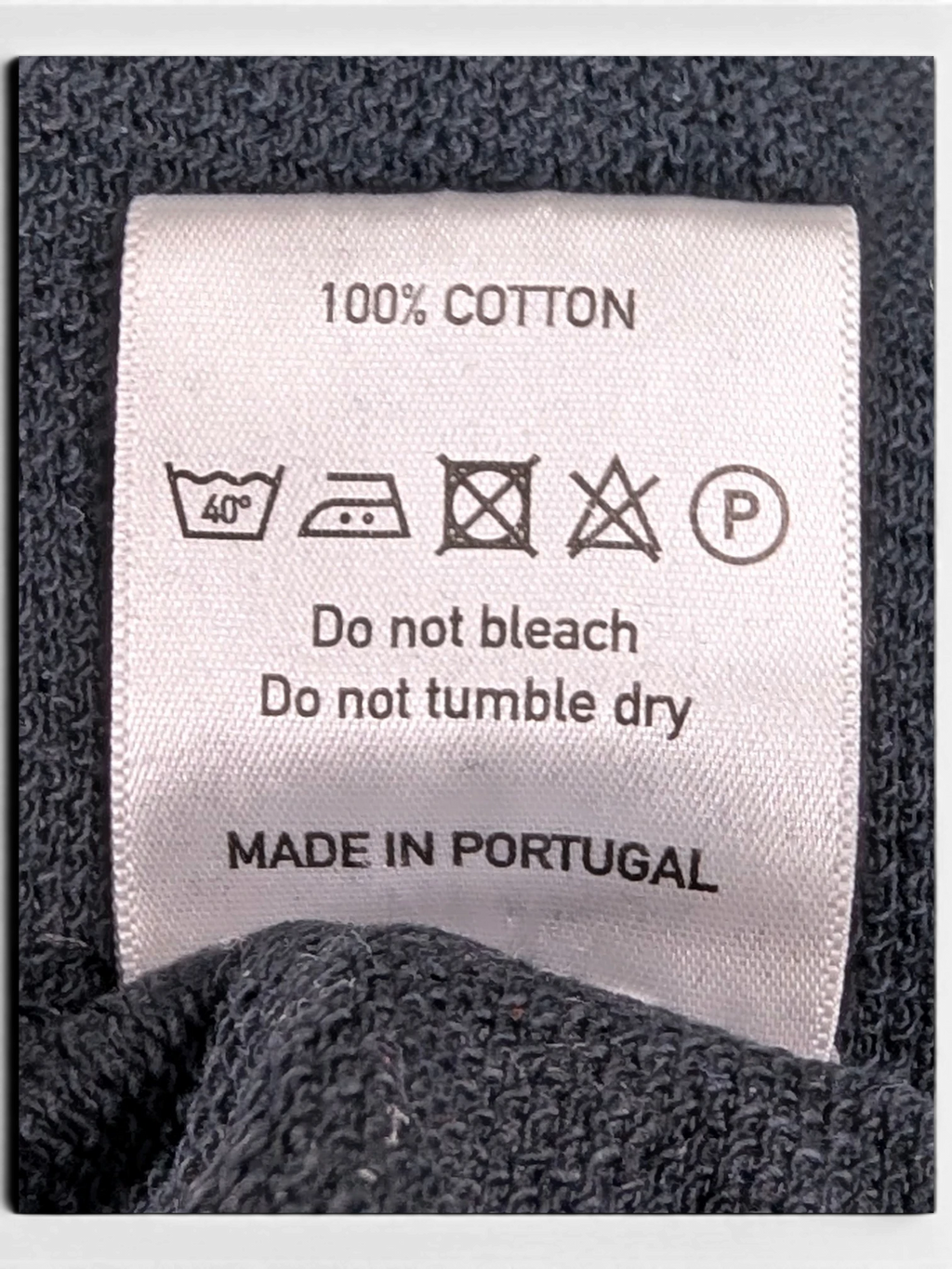 JAKE & IPI 100% cotton clothing care label with washing instructions and Made in Portugal text on dark fabric