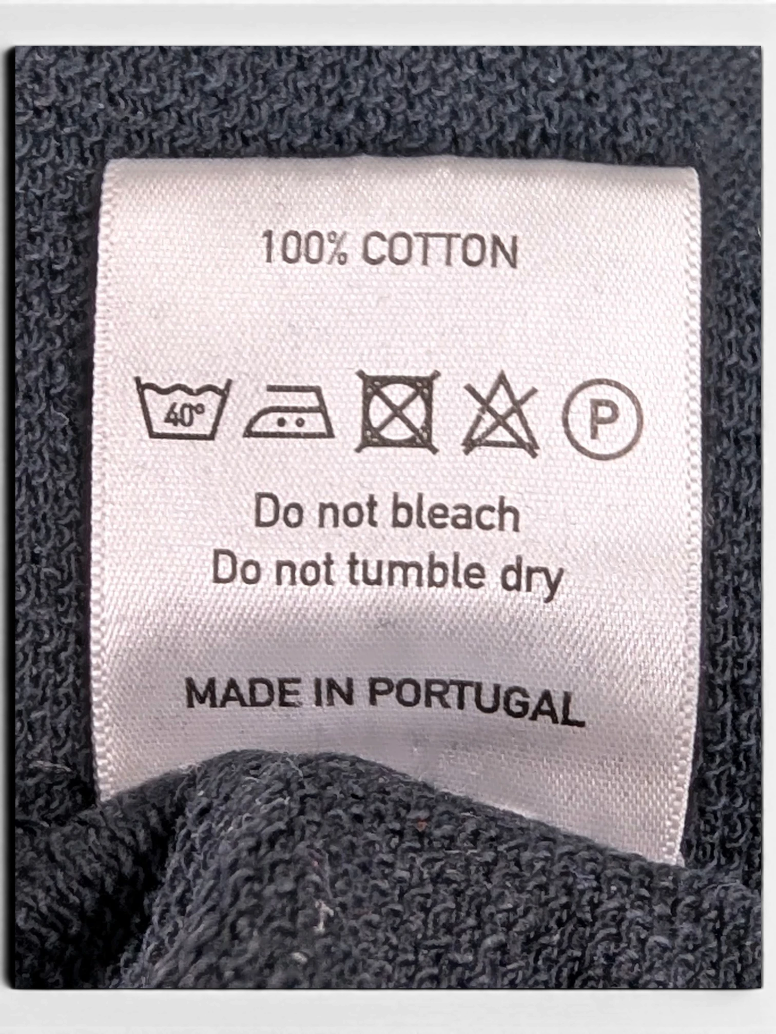 JAKE & IPI 100% cotton clothing care label with washing instructions and Made in Portugal text on dark fabric
