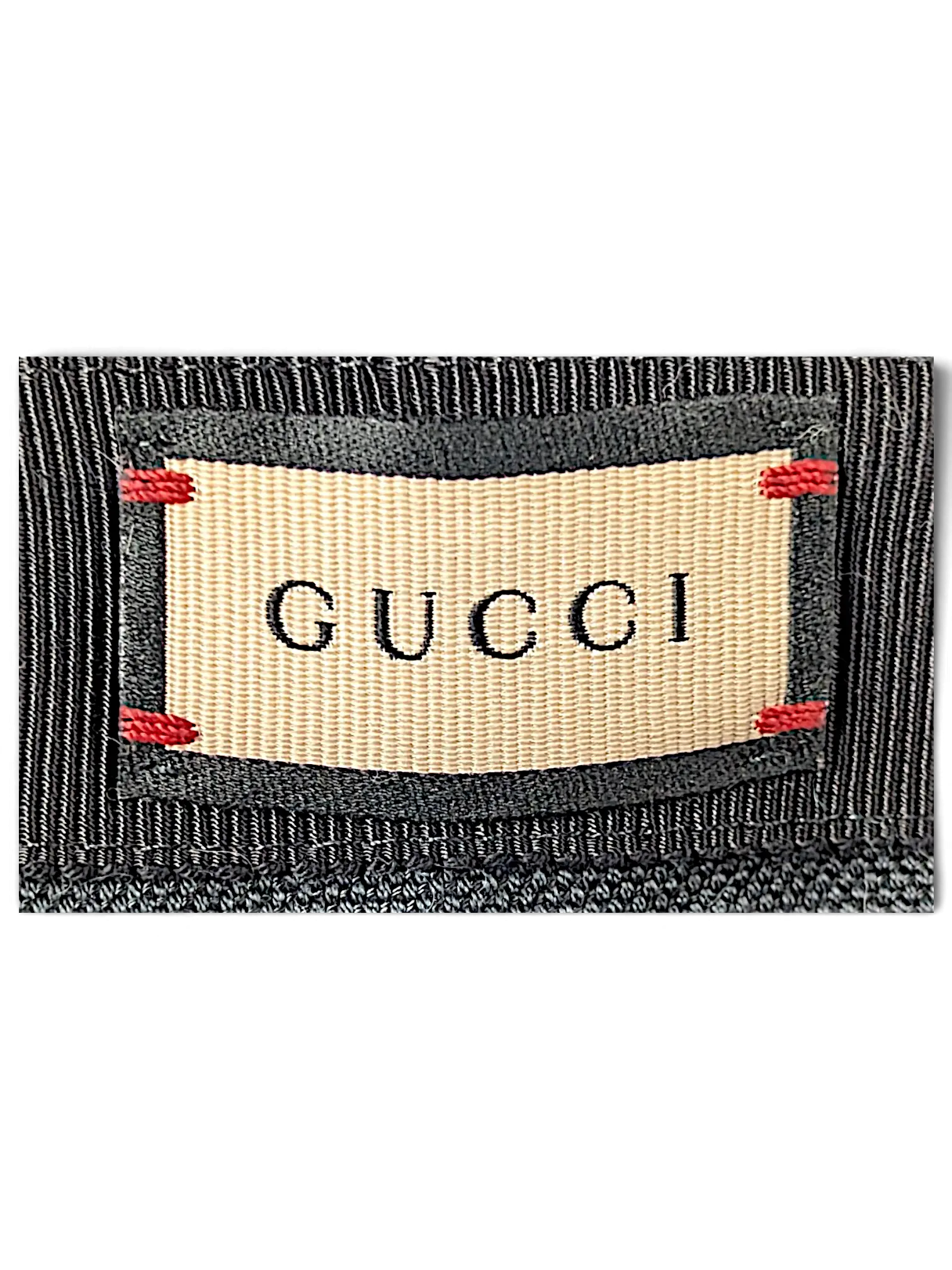 Close-up of the JAKE & IPI Gucci bucket hat brand label featuring beige fabric with black trim and red stitching.