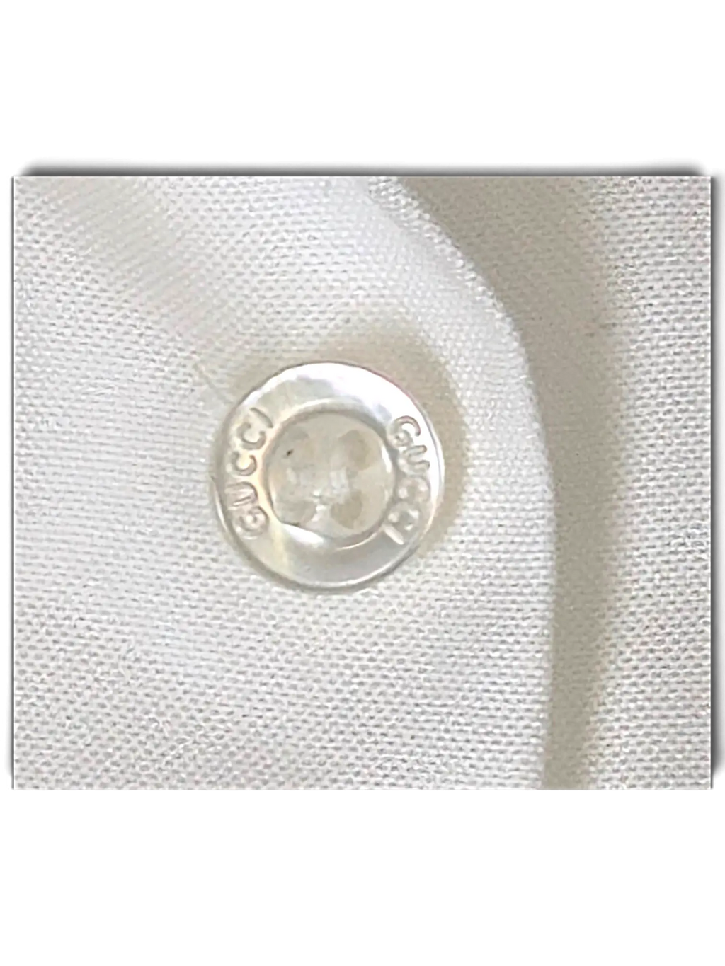 Close-up of a white JAKE & IPI Gucci shirt featuring a branded mother-of-pearl button with engraved Gucci logo.