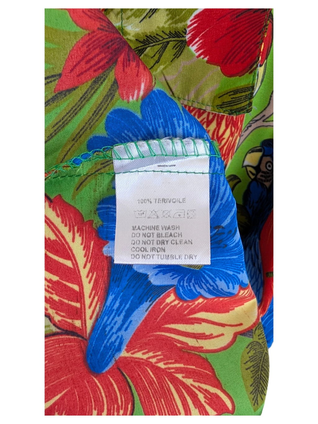 JAKE & IPI V.H.O Hawaiian shirt featuring a vibrant green, red, and blue tropical floral and parrot print fabric label