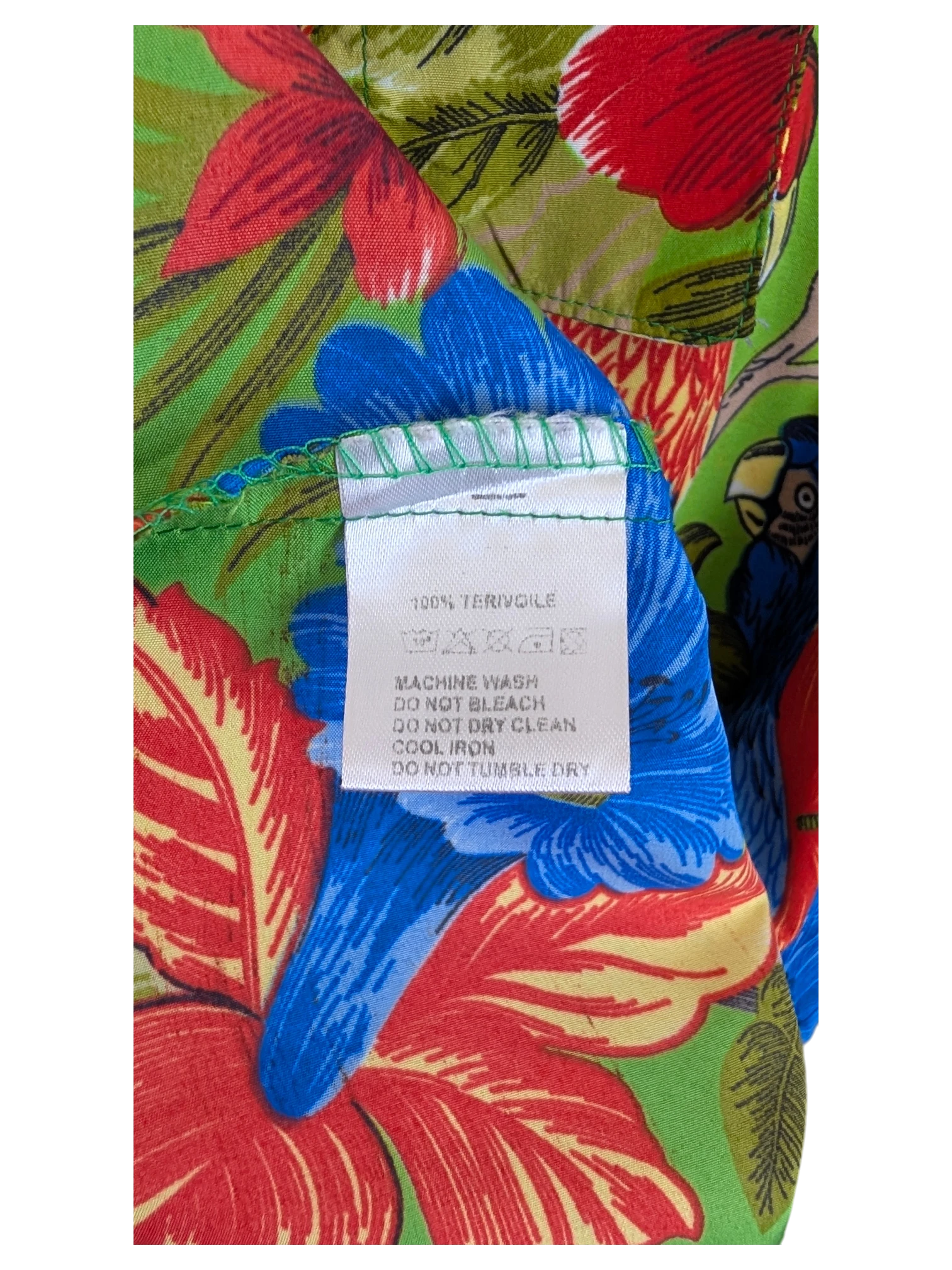 JAKE & IPI V.H.O Hawaiian shirt featuring a vibrant green, red, and blue tropical floral and parrot print fabric label