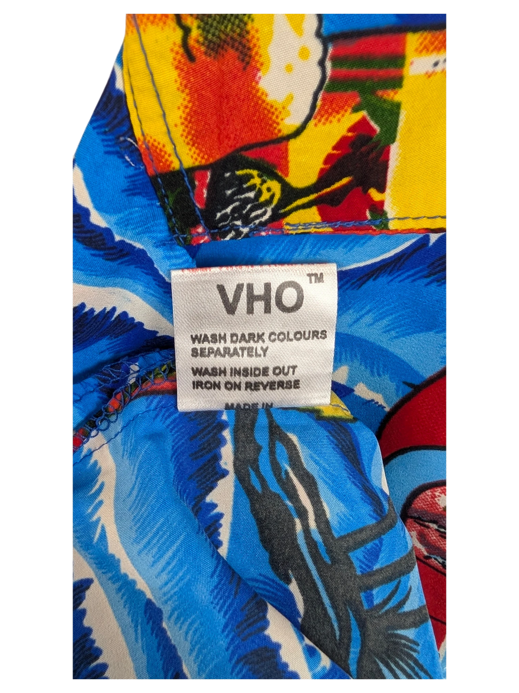 JAKE & IPI V.H.O Hawaiian shirt care label on a vibrant blue and yellow tropical floral fabric background