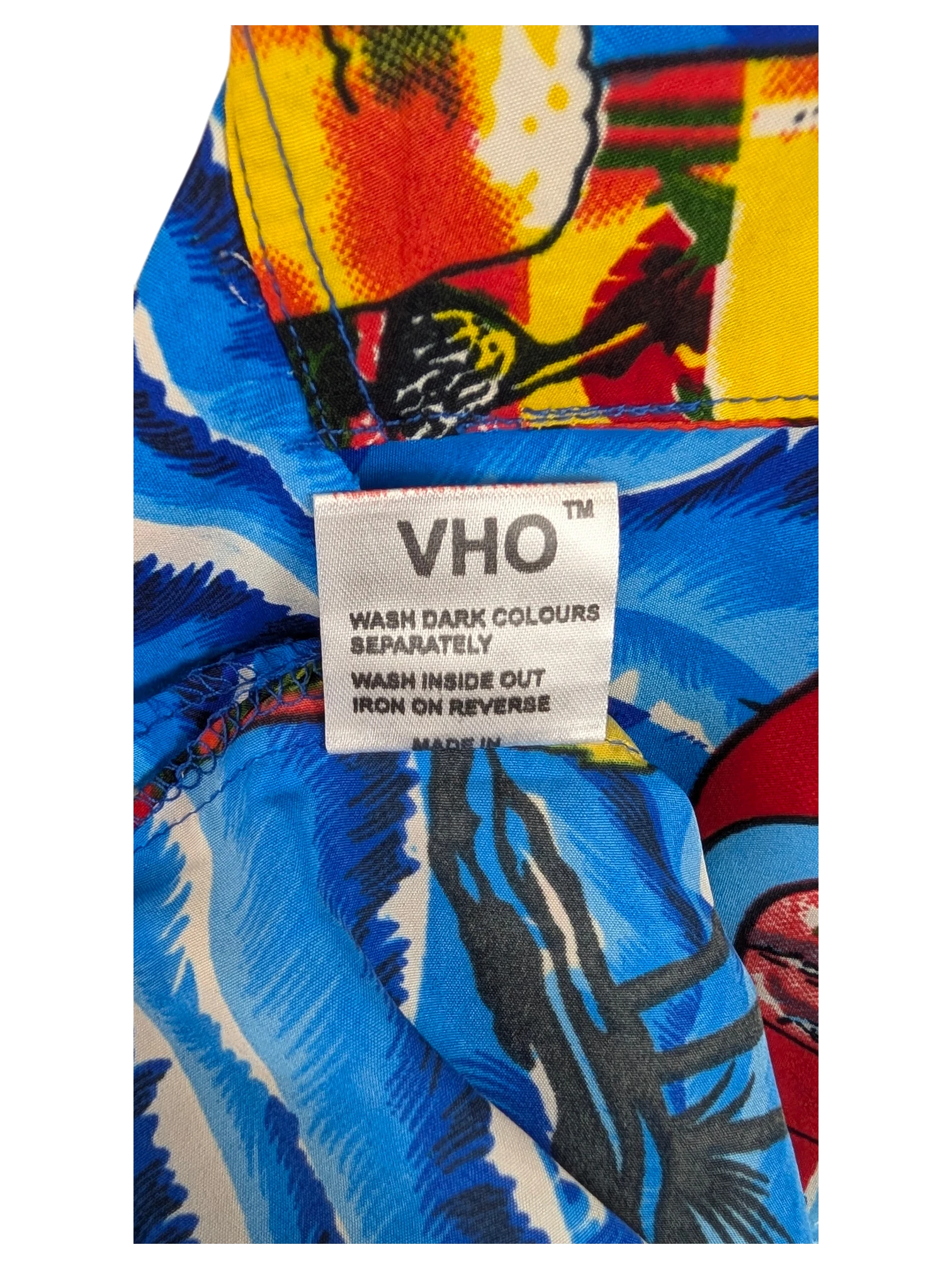 JAKE & IPI V.H.O Hawaiian shirt care label on a vibrant blue and yellow tropical floral fabric background