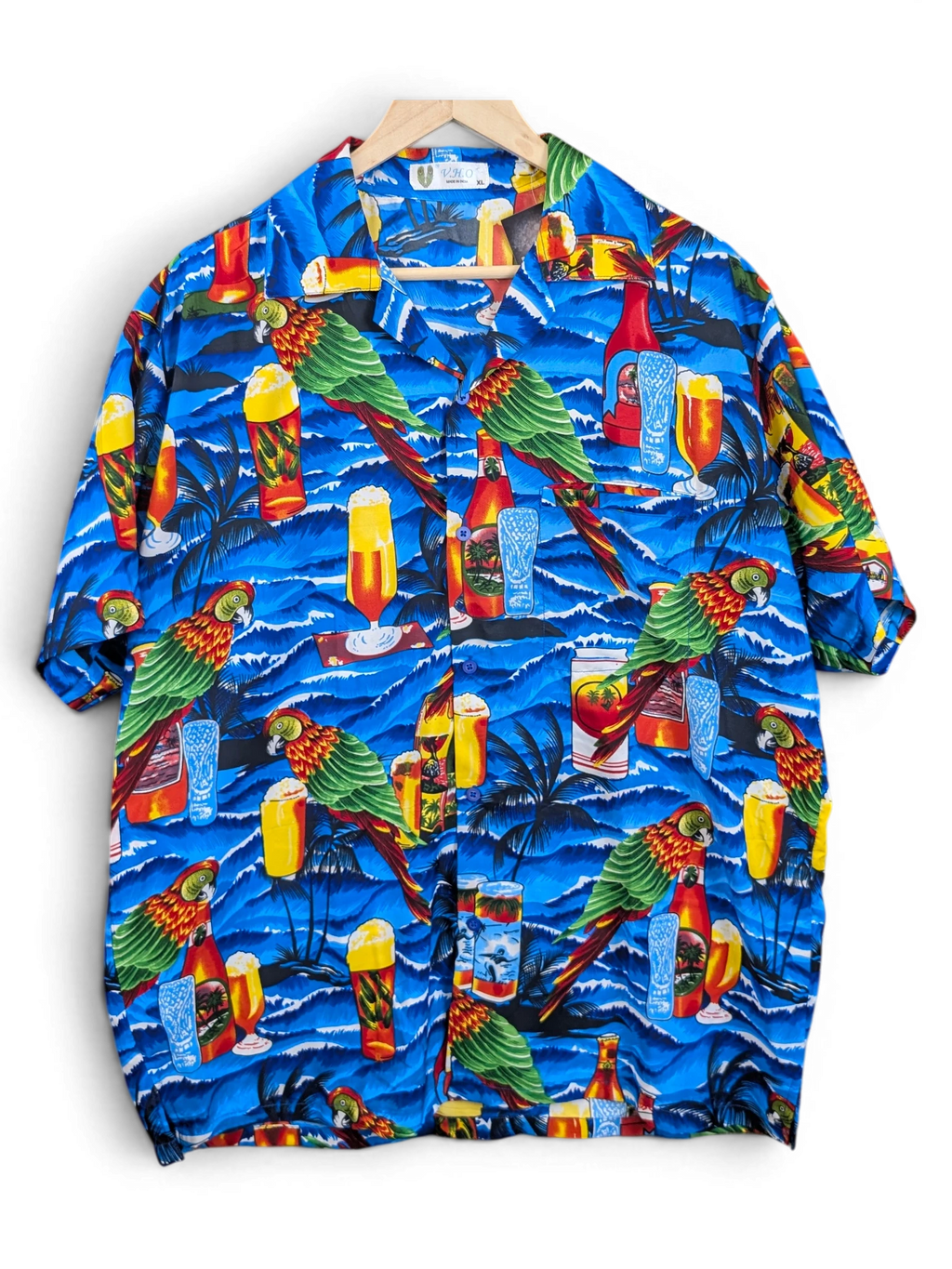 JAKE & IPI V.H.O Hawaiian shirt featuring a vibrant blue tropical print with parrots, palm trees, and beer glasses.