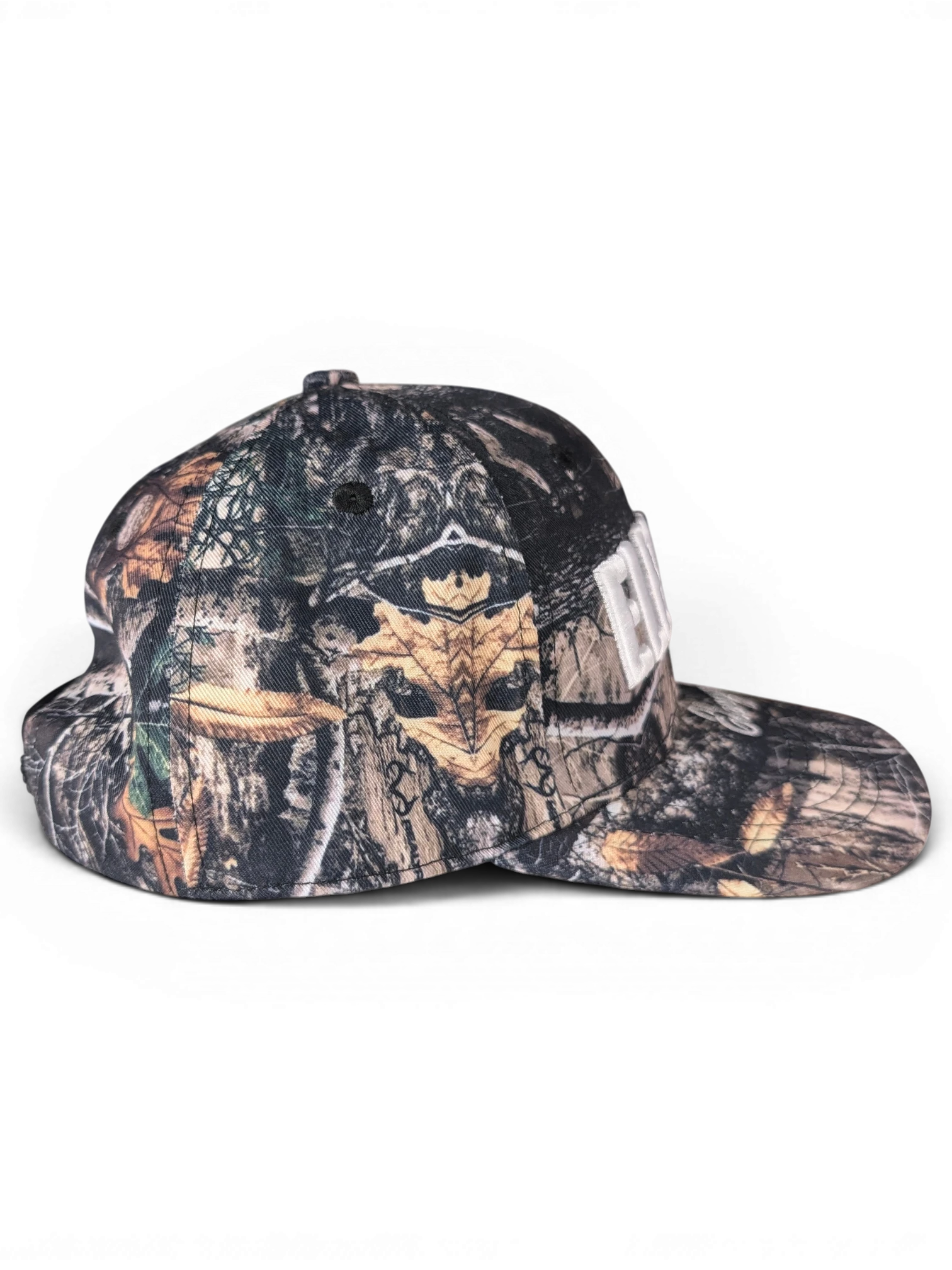 JAKE & IPI IBE Elenyor cap featuring a woodland camouflage pattern with a white embroidered logo on the front.