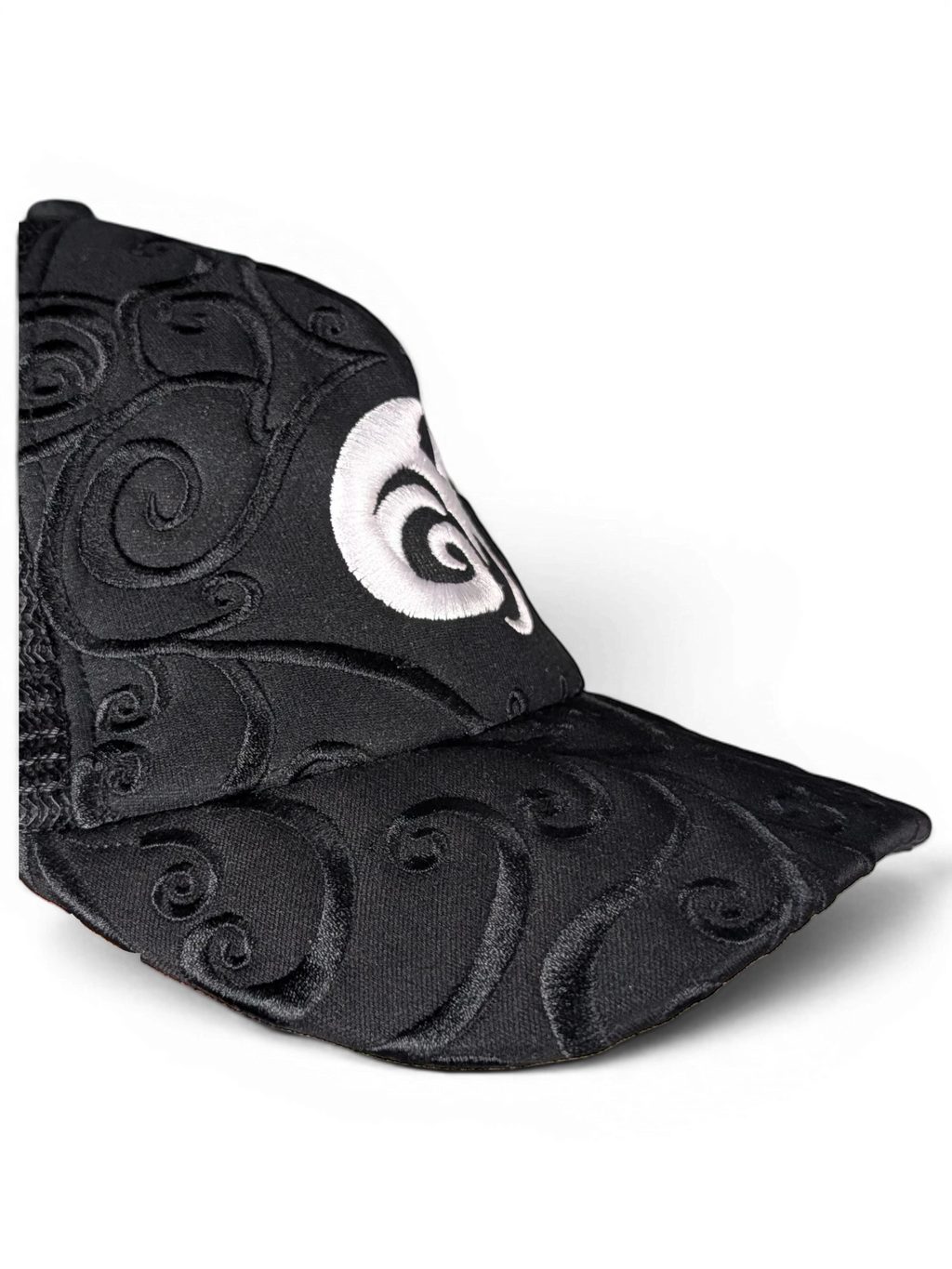 JAKE & IPI IBE Morivelle cap in black with intricate tonal embroidery and a prominent white circular logo detail