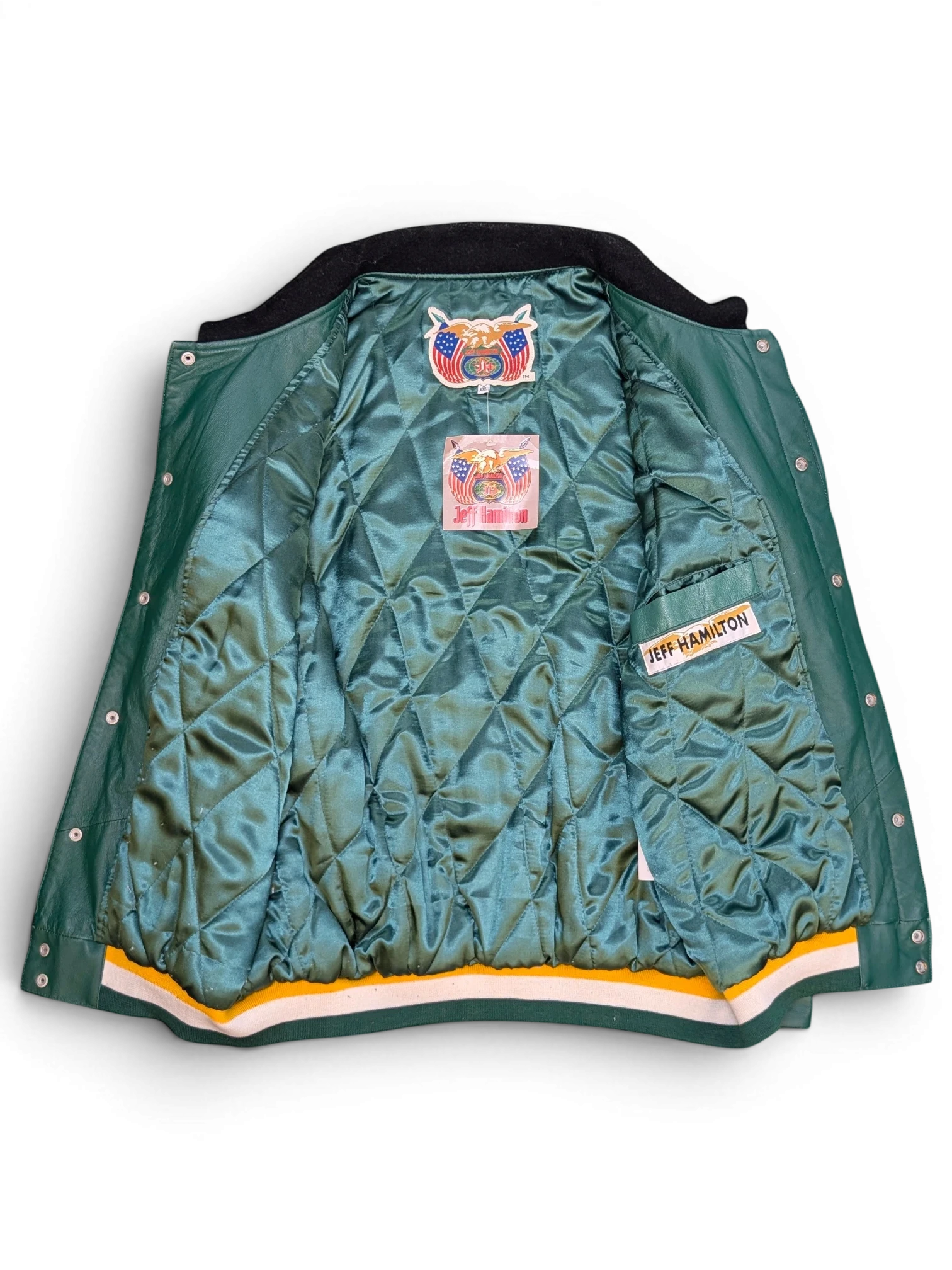 JAKE & IPI Jeff Hamilton varsity jacket interior with green quilted lining, branded labels, and striped hem.