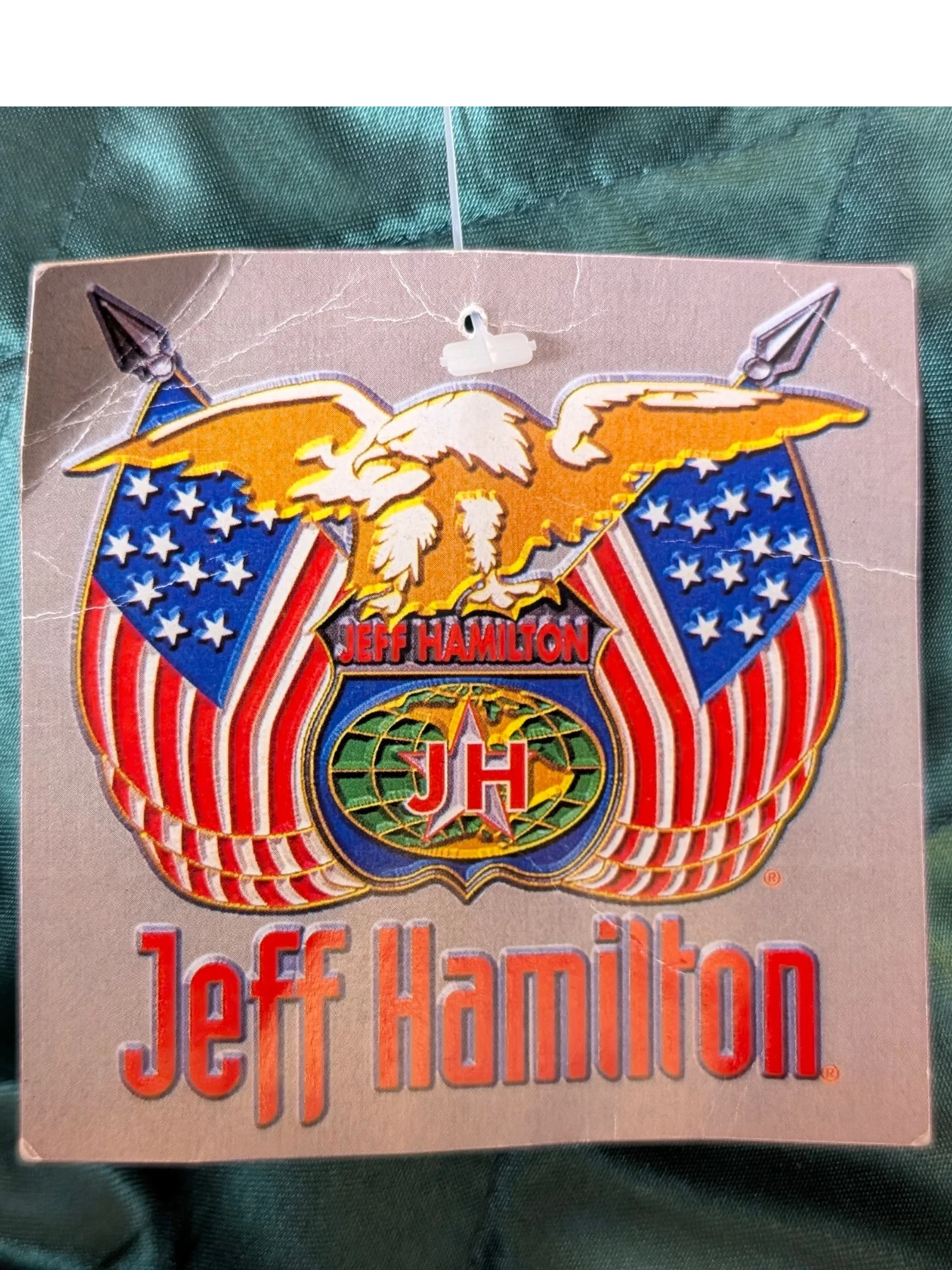 JAKE & IPI Jeff Hamilton varsity jacket tag featuring an eagle, American flags, and JH logo on a green satin fabric