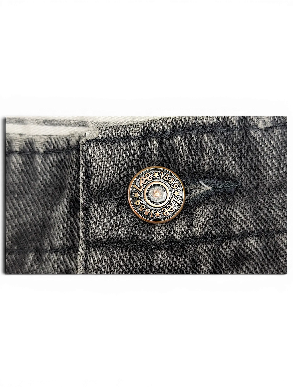 Close-up of a JAKE & IPI Lee stretch waist jeans button in antique bronze finish on dark grey denim fabric.