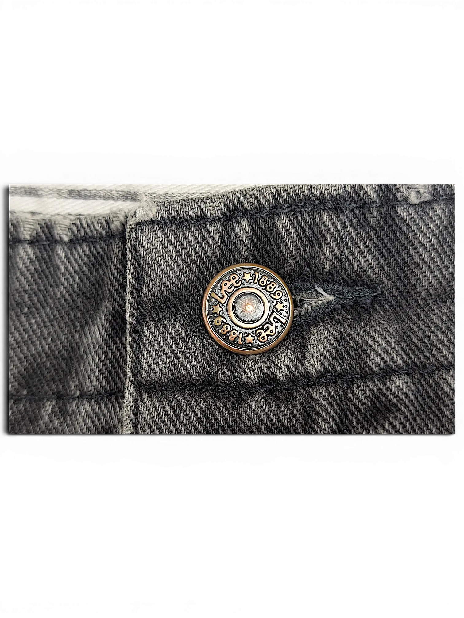 Close-up of a JAKE & IPI Lee stretch waist jeans button in antique bronze finish on dark grey denim fabric.