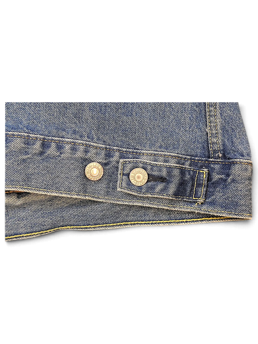 Close-up of JAKE & IPI Levi's denim jacket hem featuring blue wash fabric, yellow stitching, and branded metal buttons.