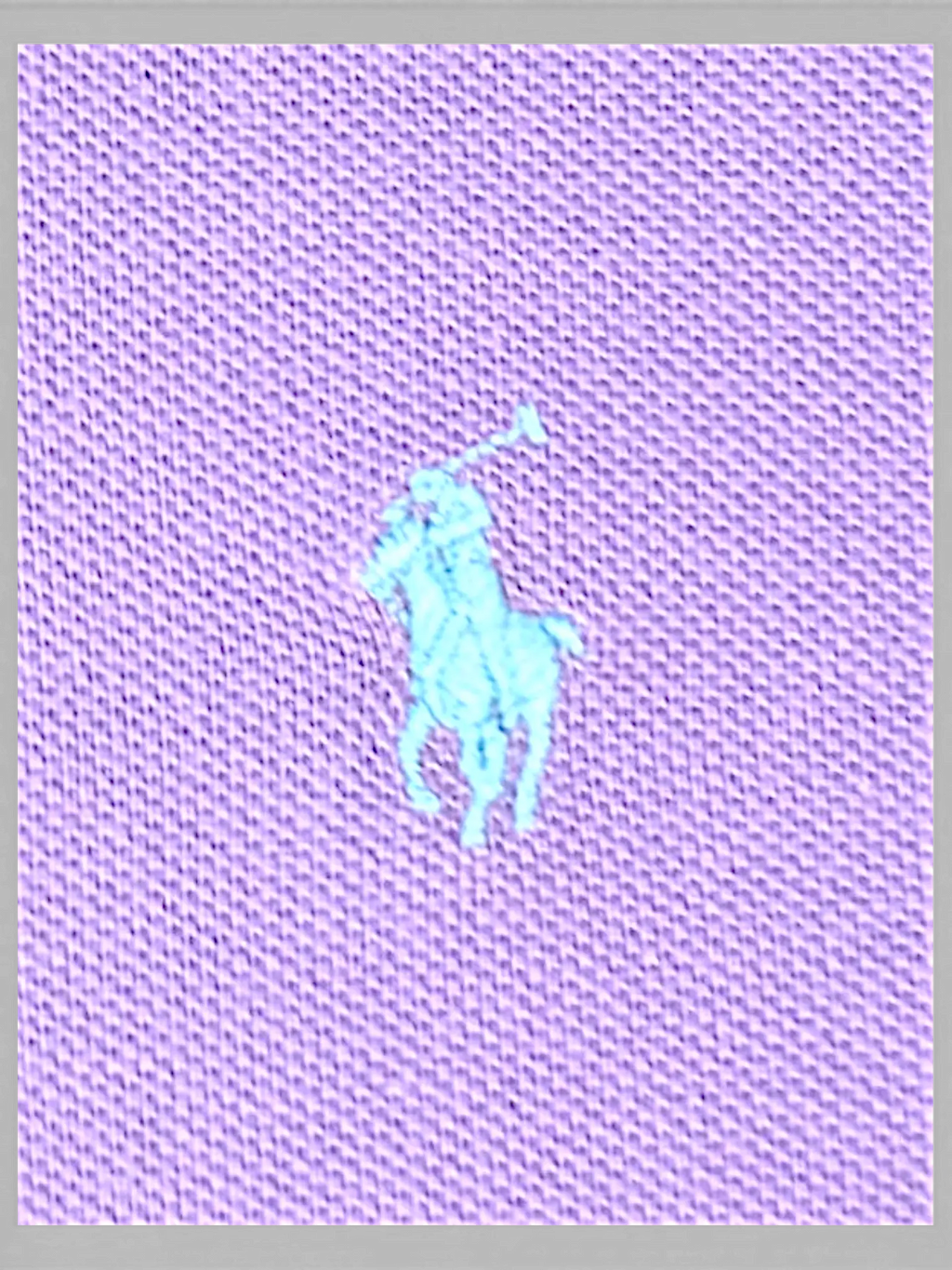 Close-up of JAKE & IPI lilac polo shirt fabric featuring an embroidered light blue polo player logo