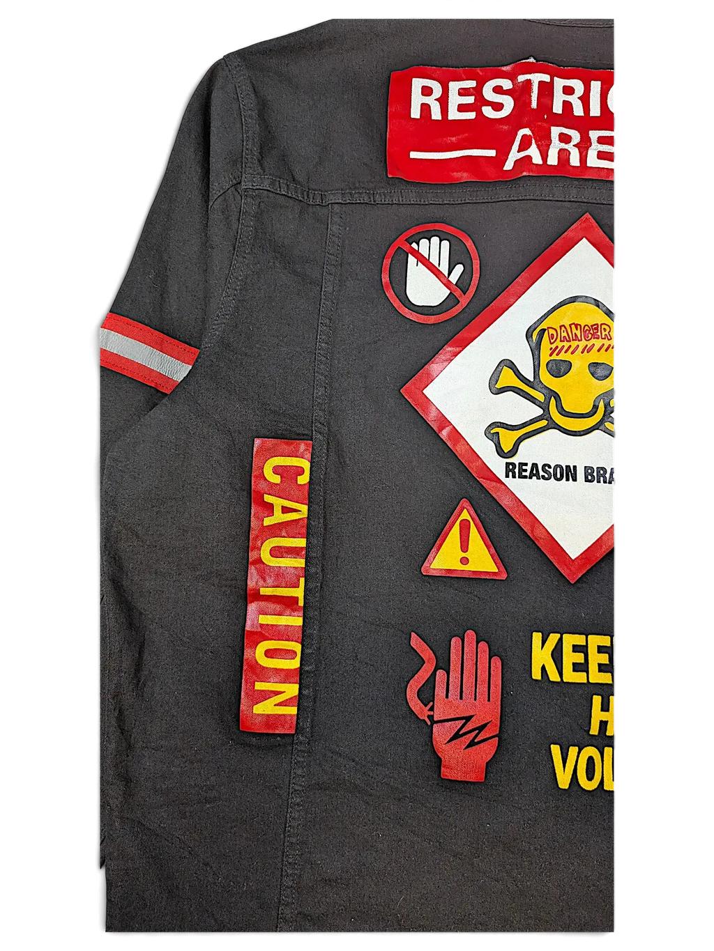 JAKE & IPI Reason denim jacket in black featuring bold red and yellow hazard-themed patches and warning graphics.