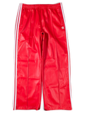 JAKE & IPI red Adidas track pants with white side stripes and embroidered logo on a green background