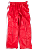 JAKE & IPI red Adidas track pants with white side stripes and embroidered logo on a green background