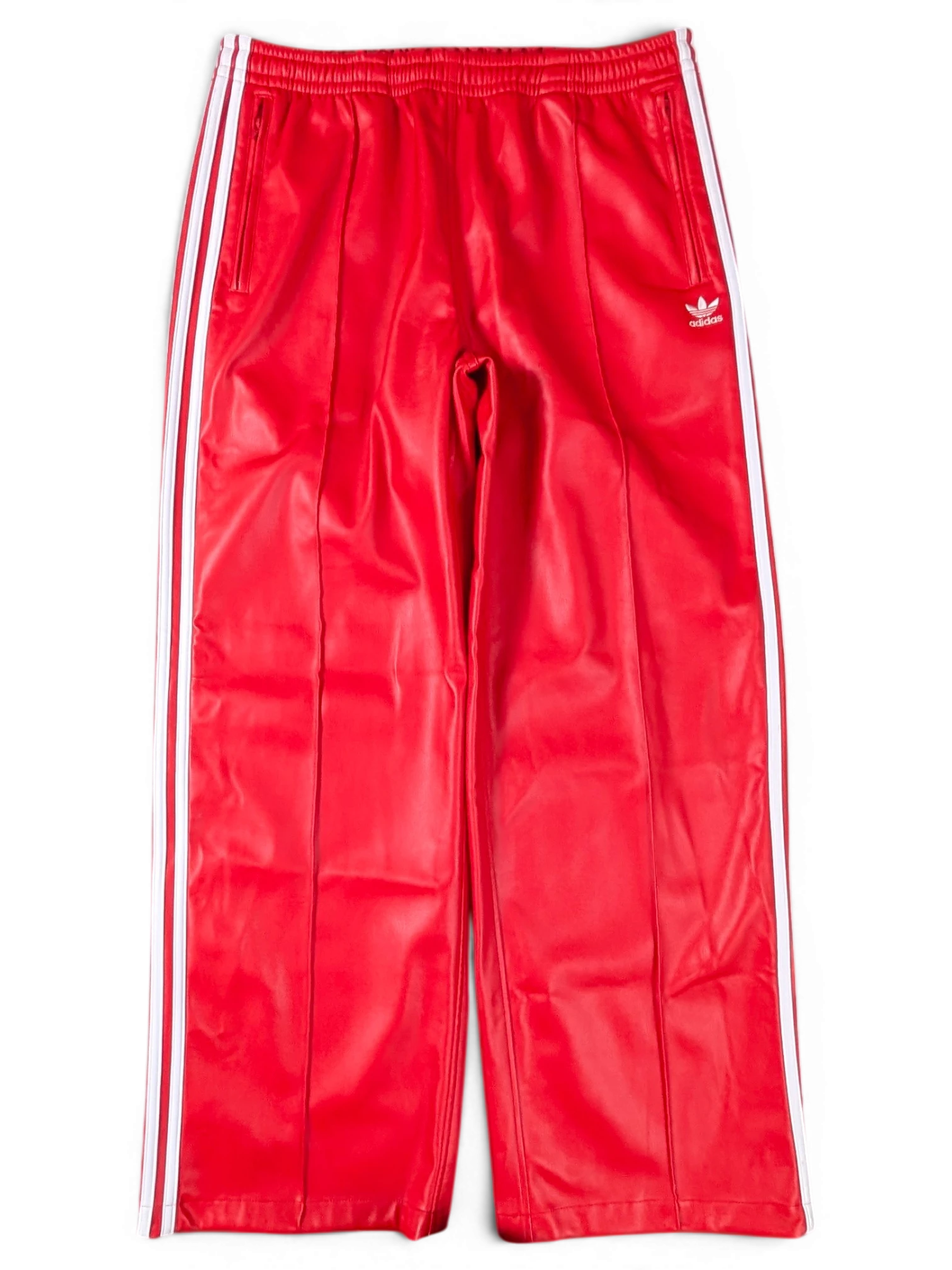 JAKE & IPI red Adidas track pants with white side stripes and embroidered logo on a green background