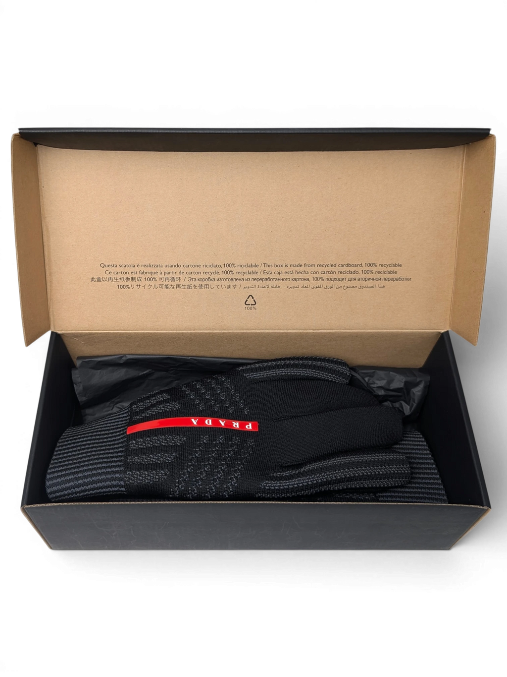 JAKE & IPI Reusch for Prada black knit gloves with red logo detail inside a recycled cardboard gift box.
