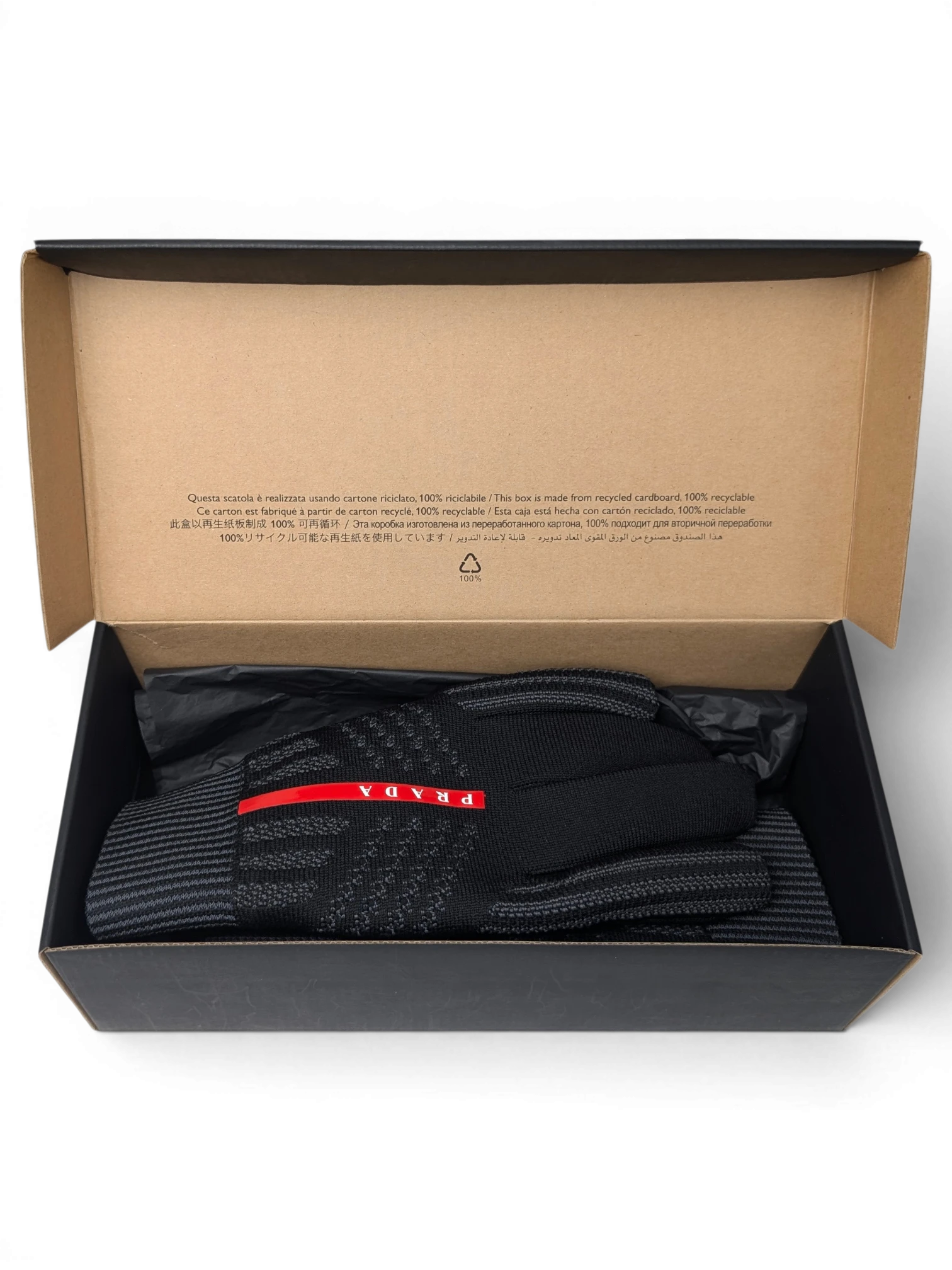 JAKE & IPI Reusch for Prada black knit gloves with red logo detail inside a recycled cardboard gift box.